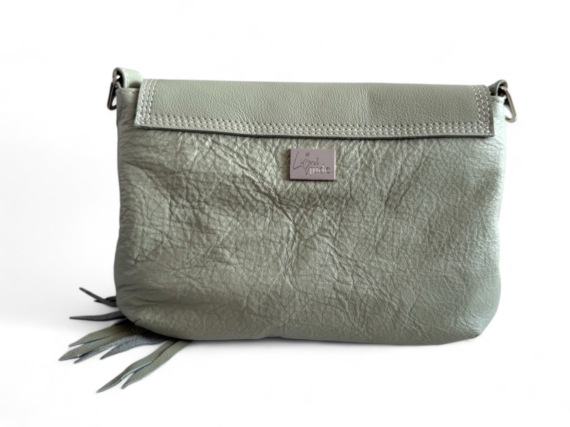 light sage green, leather crossbody bag. The view is of the back of the bag and shows the silver Lilly & Jude logo badge and the stitching on the back of the flap. This one-off bag is shown on a white background