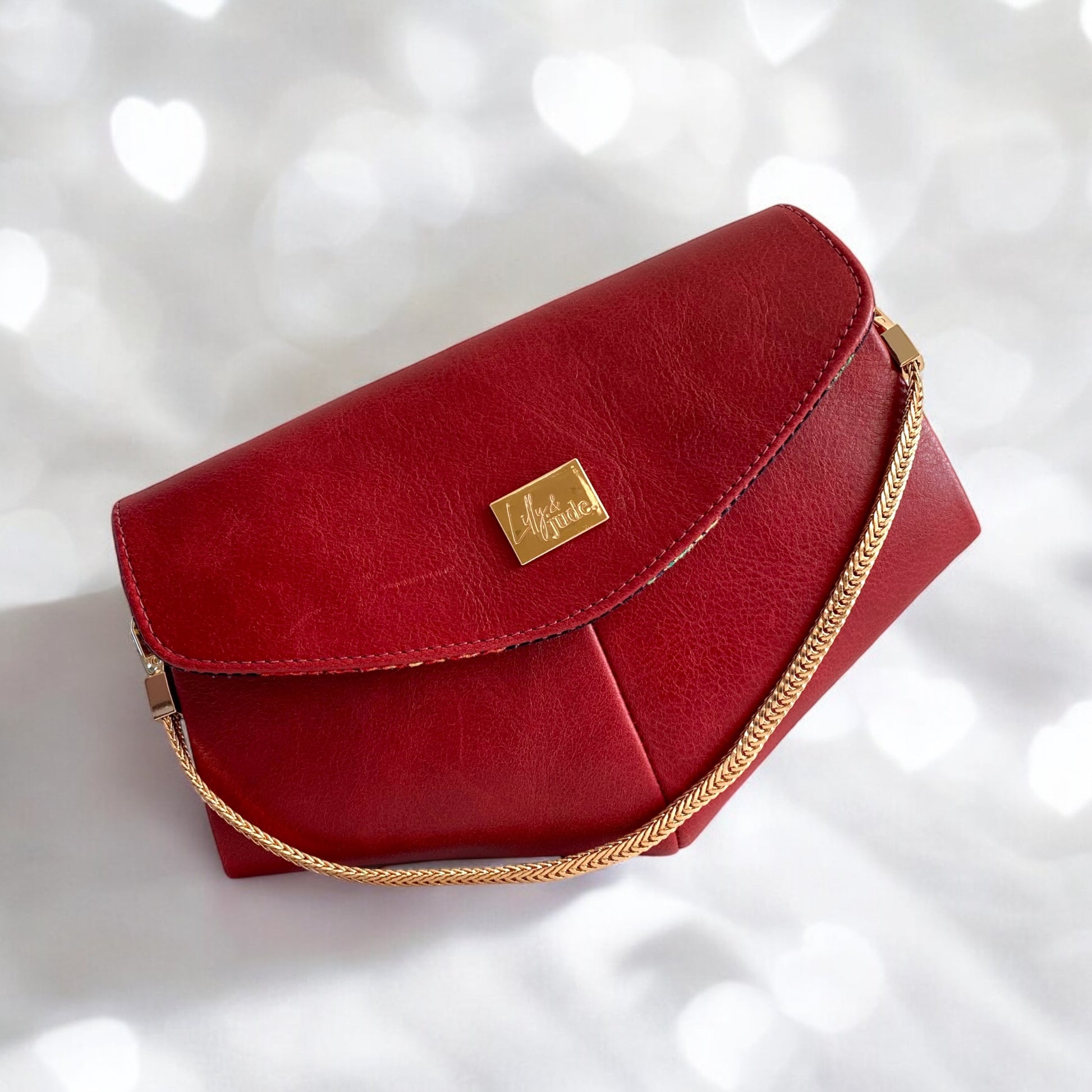 Beautiful triangular bottomed clutch bag, made from genuine red leather that has been rescued from heading the landfill. The handbag has a gold Lilly & Jude logo plate and a gold chain handle