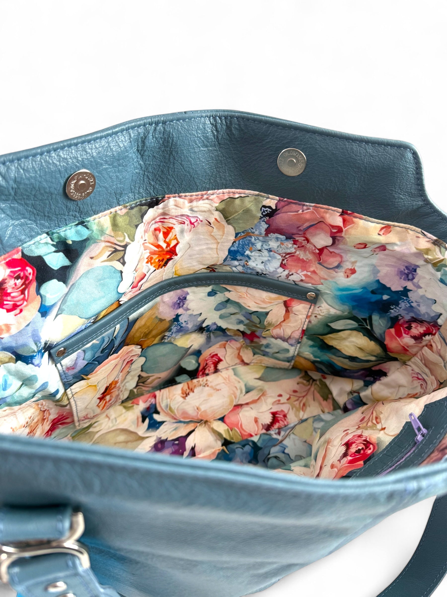 Interior of a handcrafted blue leather handbag with a floral fabric lining and a matching leather-trimmed slip pocket, made in Shropshire by Lilly & Jude
