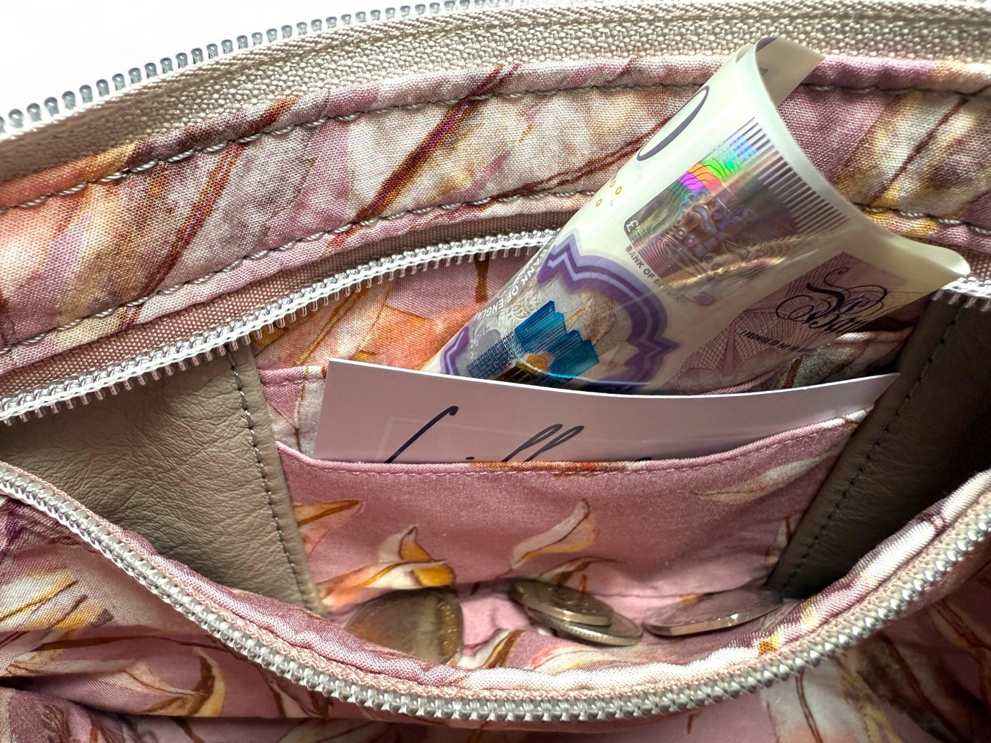 View of inside the Starburn bag, showing the built-in purse, which has card slots and space for cash and coins. It is secured inside the zipper pocket. The lining is a dusty pink with a leaf pattern