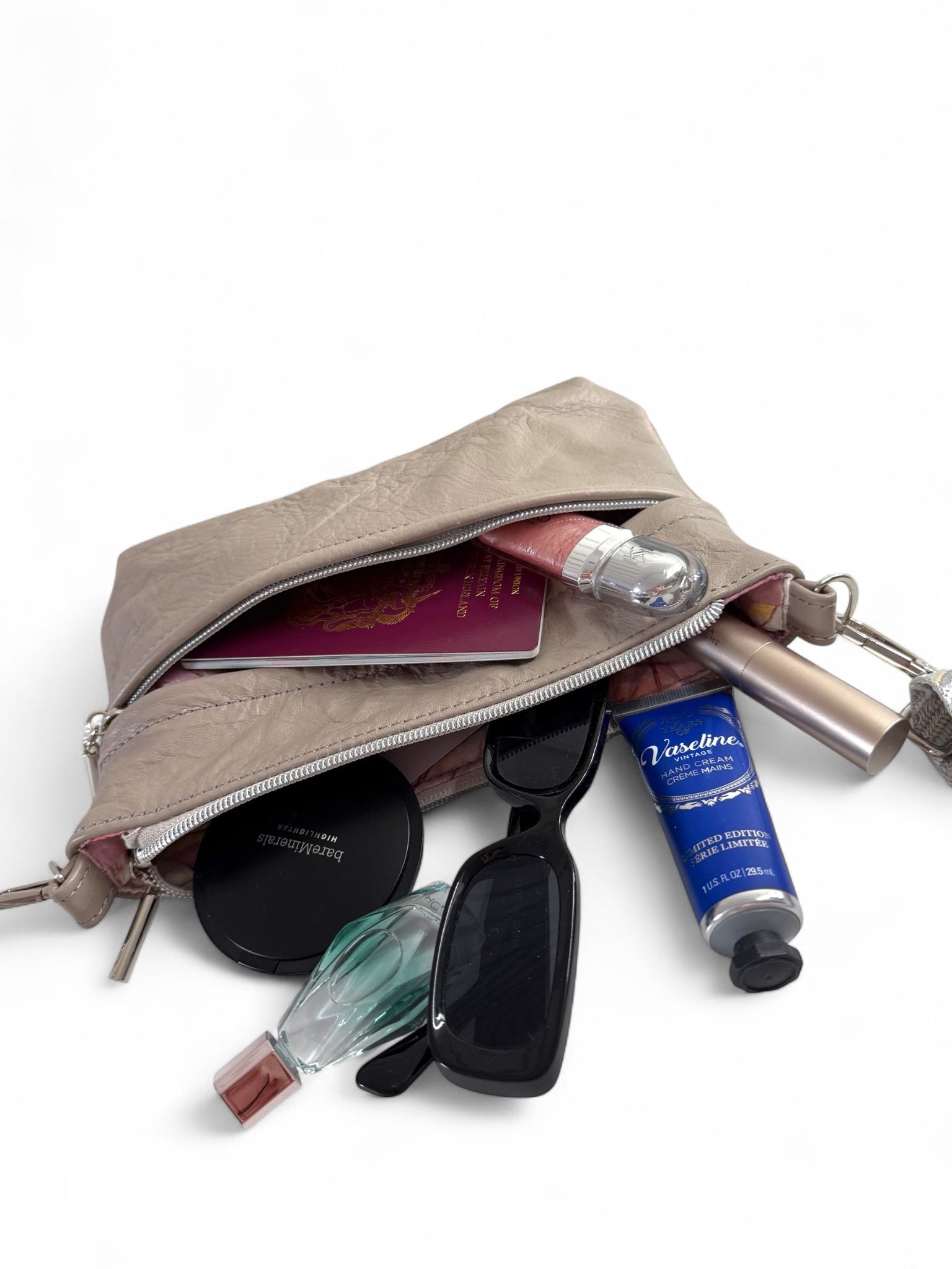 Grey leather crossbody bag with contents spilling out on a white background. Every day bag.