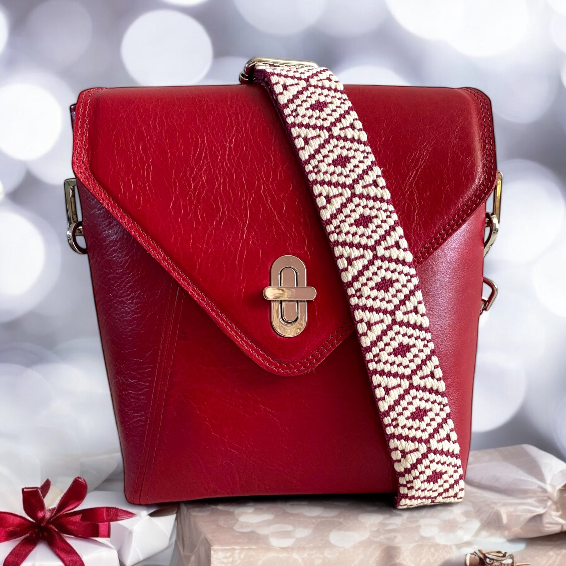 The SWALK deep red leather crossbody bag by Lilly & Jude, shown against a bokeh-lit background with a matching red bow gift box.