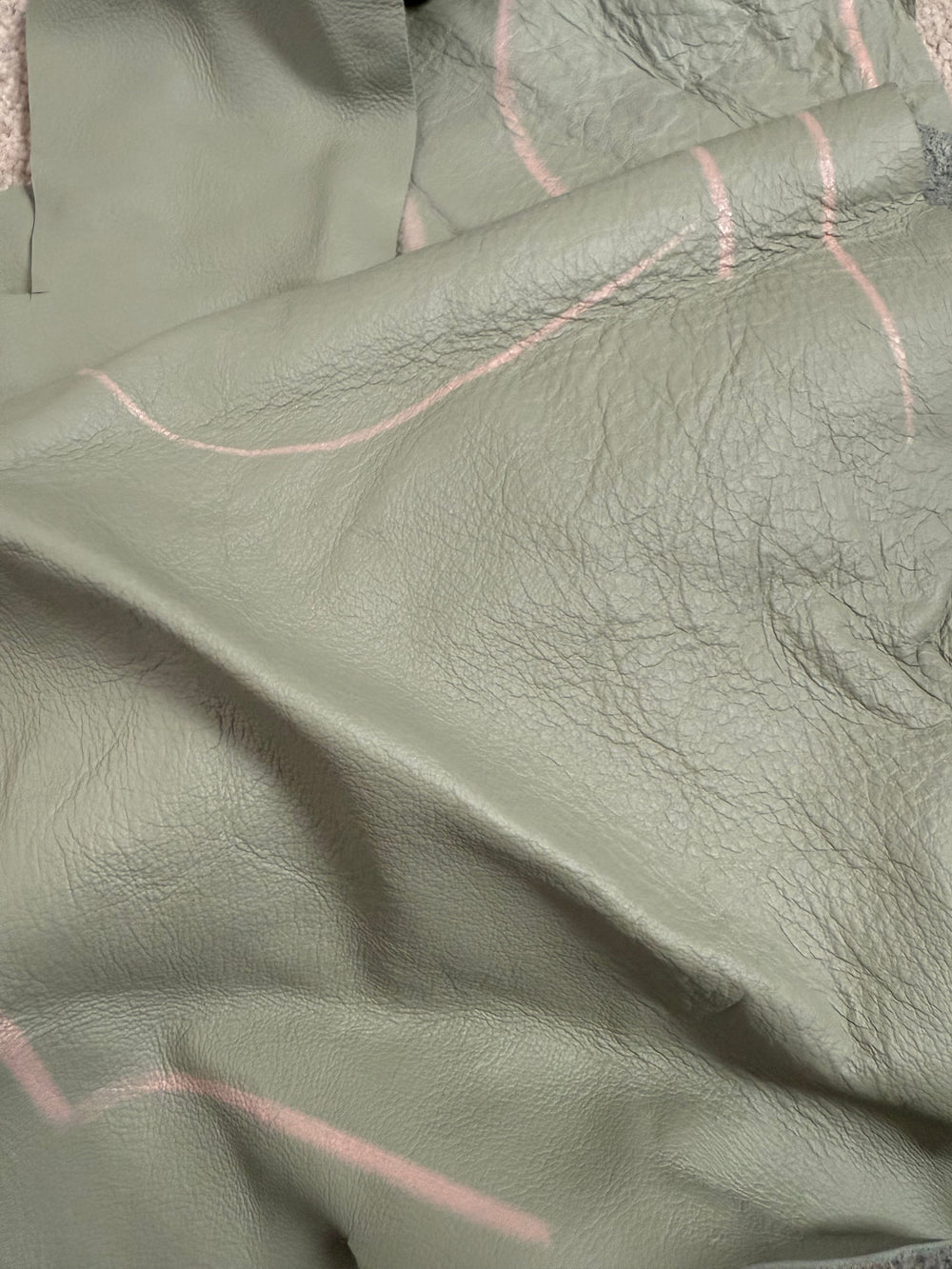 Close-up of a natural leather hide with wrinkles and chalk markings, showing the unique texture and character of rescued leather used in Lilly & Jude bags.
