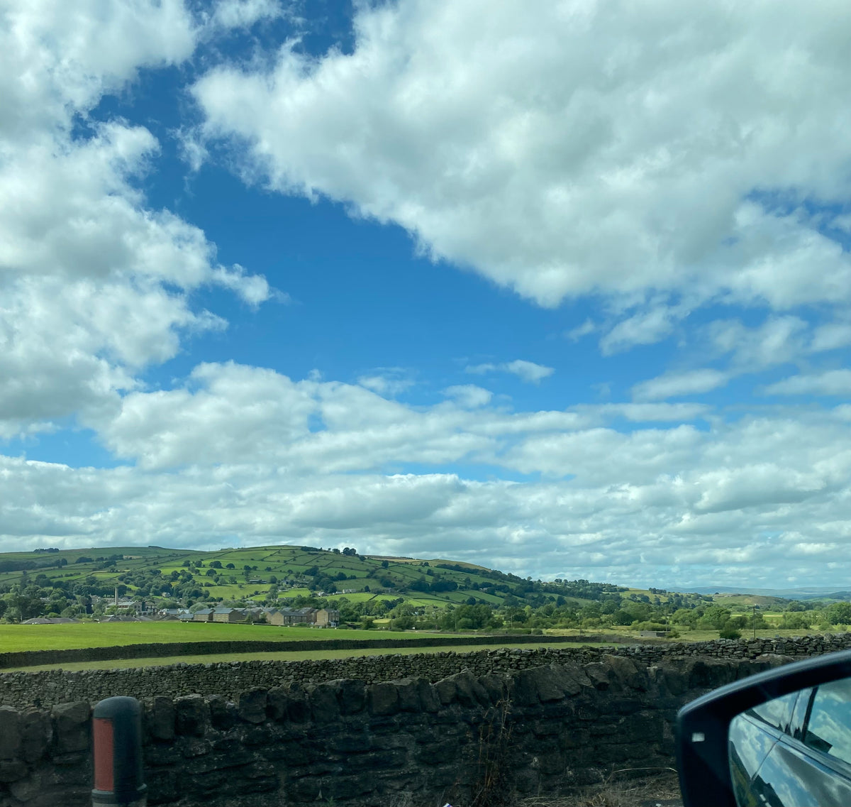 View from inside a car looking out over the lush green Yorkshire Moors with stone walls and a blue sky – peaceful creative thinking spot.