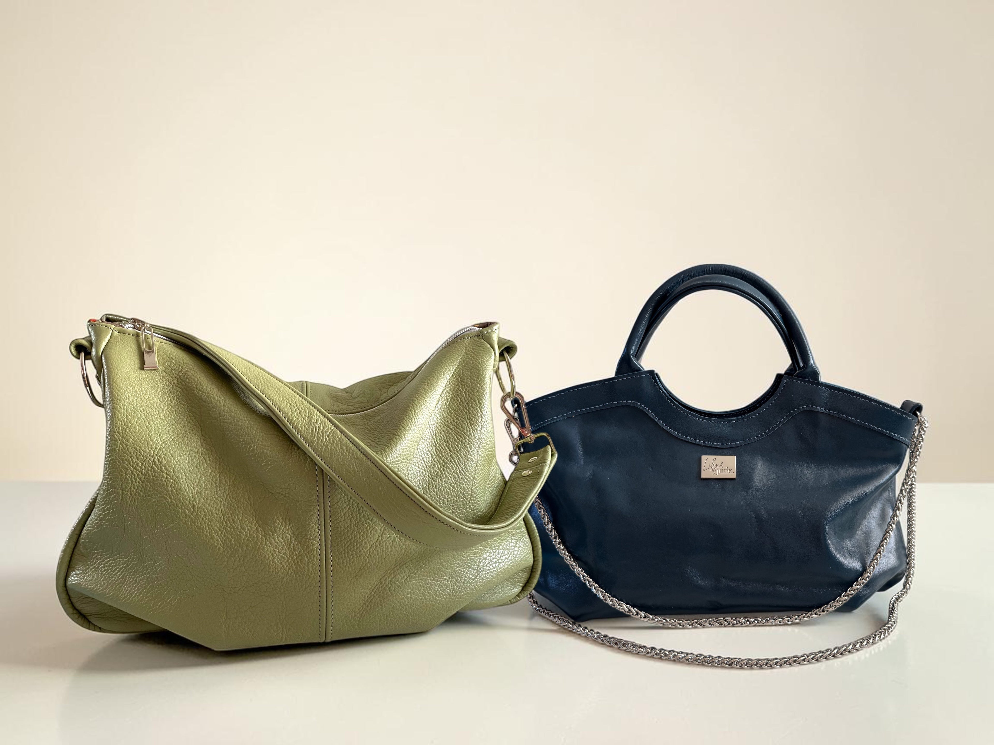 An olive green leather hobo bag and a navy blue handbag with a silver chain on a neutral background