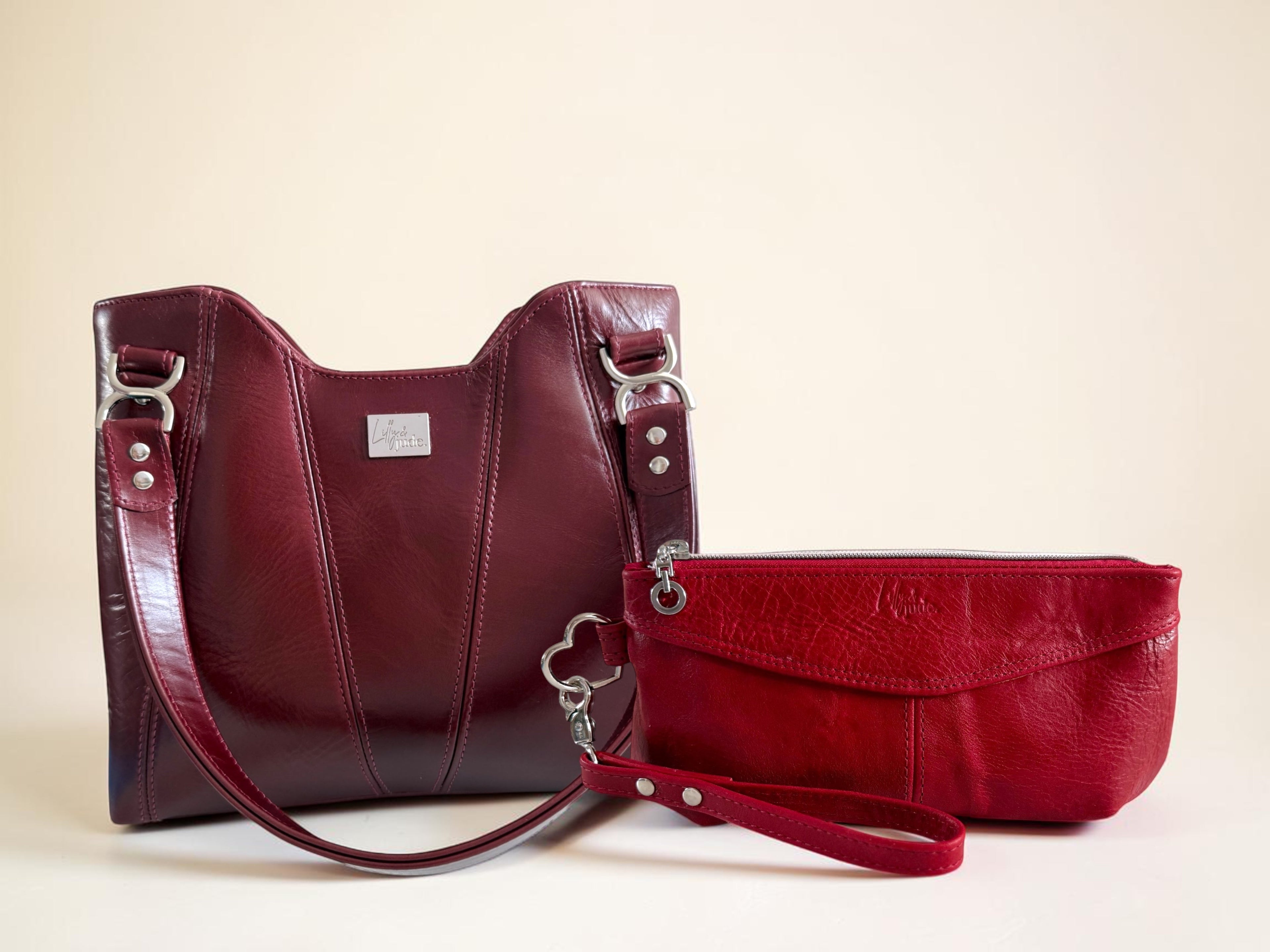 A burgundy leather handbag with a red leather wristlet on a neutral background