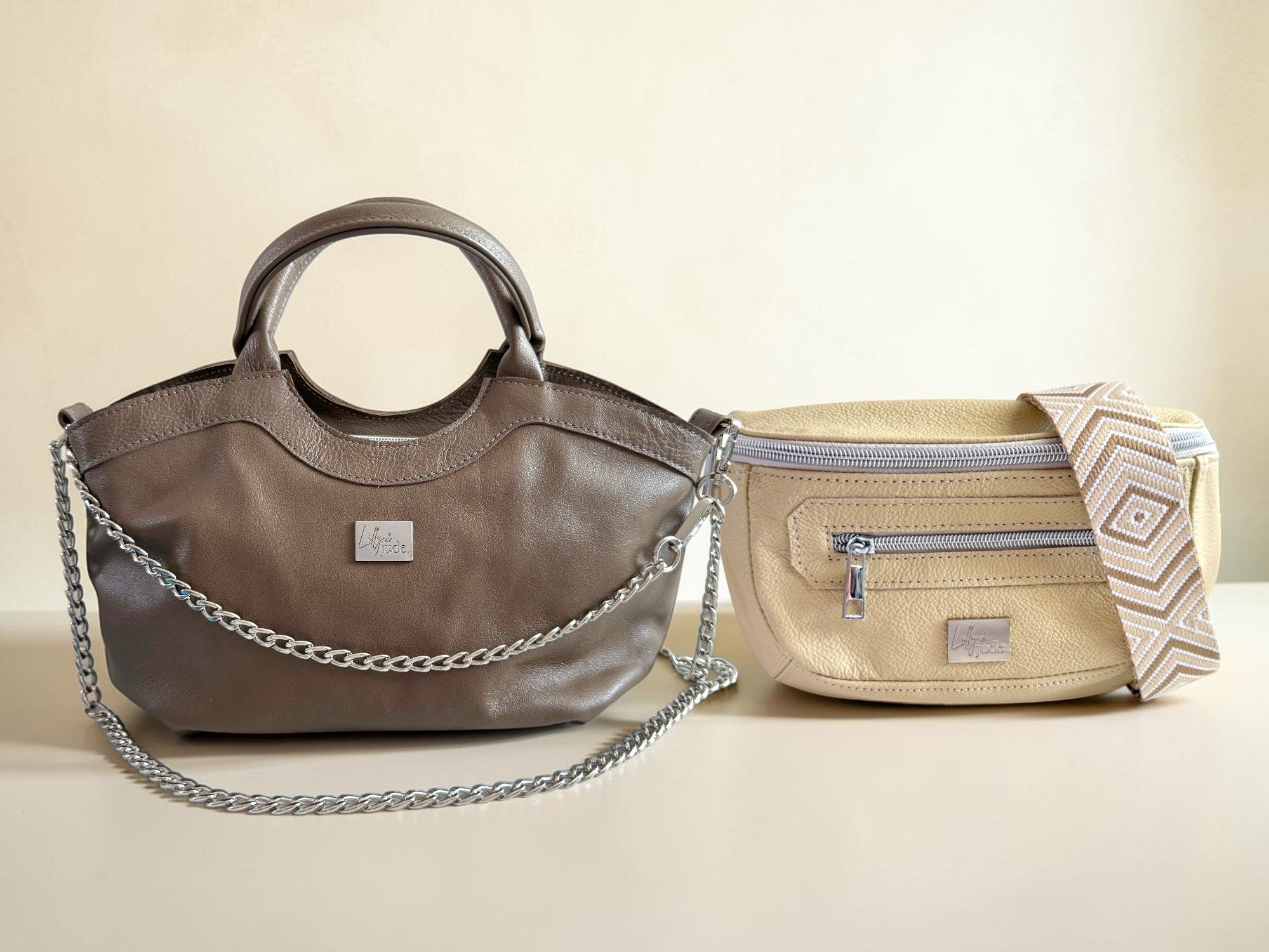 A taupe leather handbag and a cream leather waist bag against a cream background