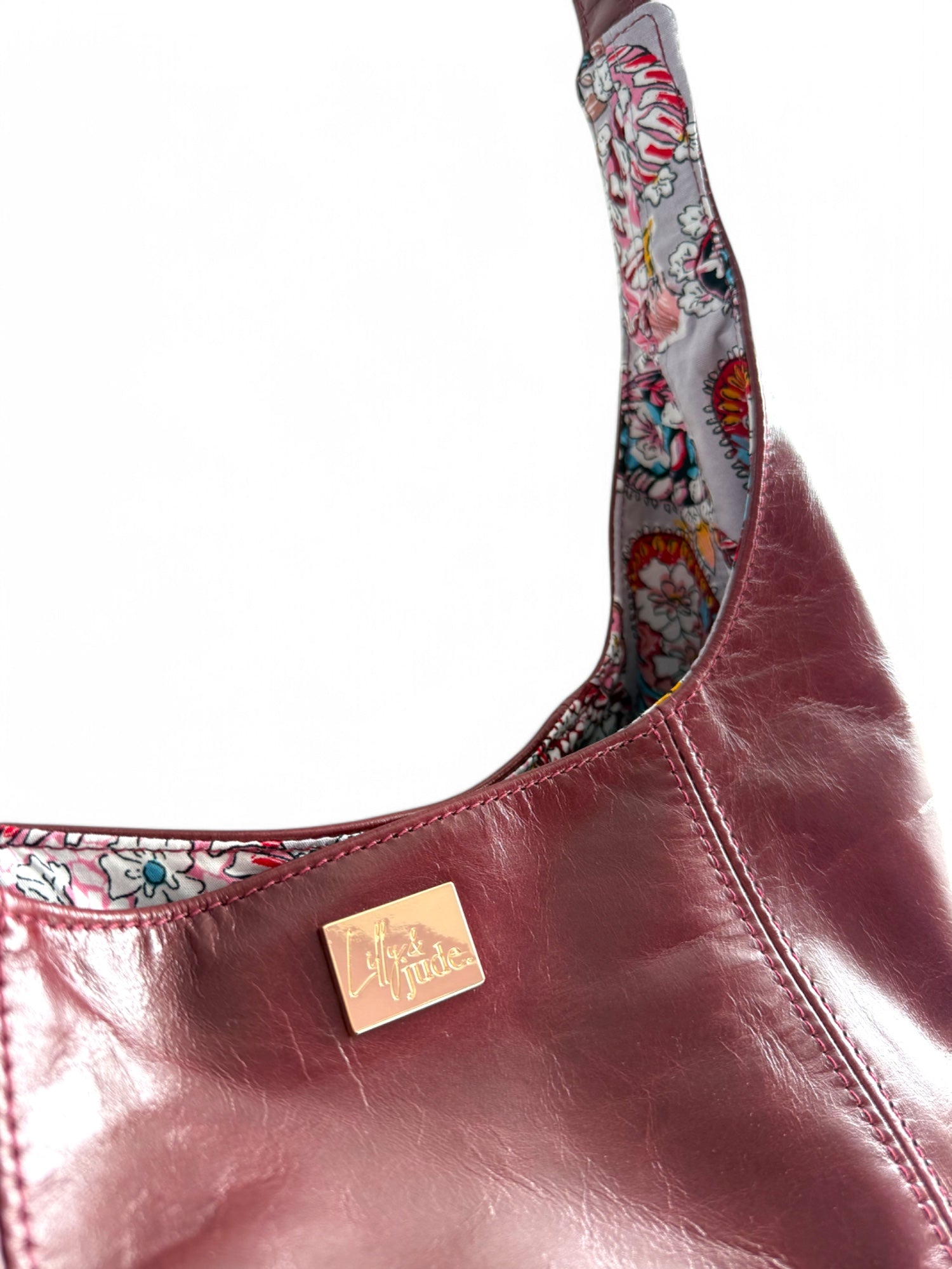 Close up details of the burgundy leather bag. It shows the stitching and gold Lilly & Jude metal logo tag