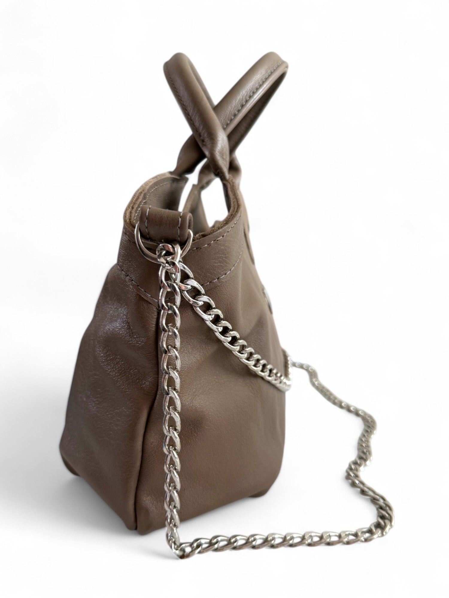 Side view of a taupe leather handbag, showing the detail of the silver chain strap detail. The slouchy bag is against a white background 