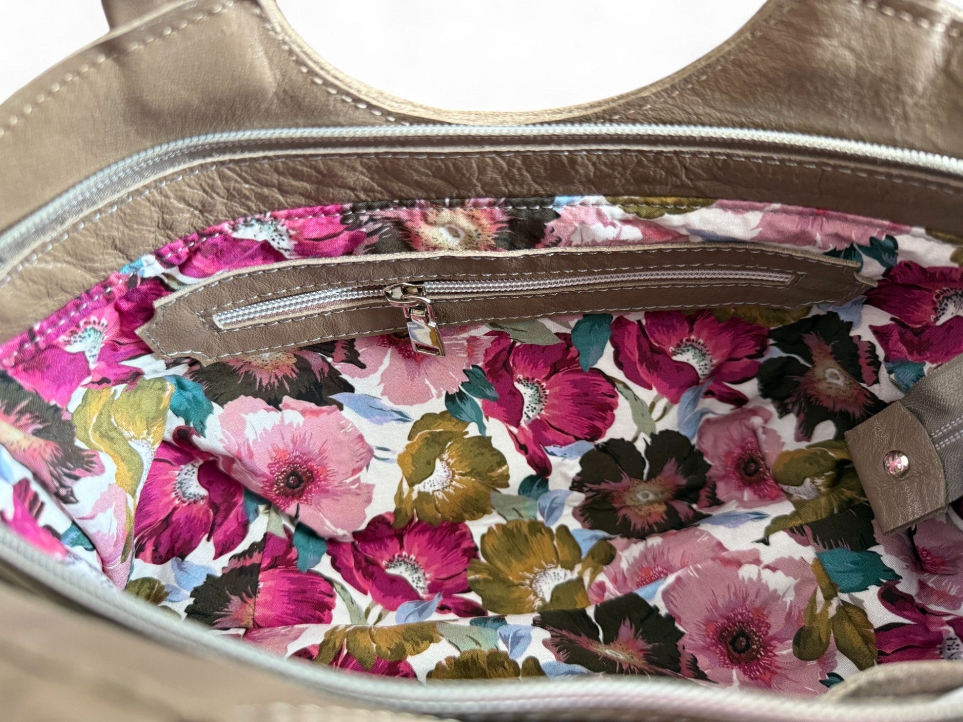 View of the interior lining of the Flossy bag. The floral lining contrasts beautifully against the taupe coloured leather. The image also shows the leather trimmed interior zipper pocket. Exclusive, one-off bag by Lilly & Jude