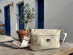 Cream leather crossbody bag with silver hardware and matching strap, sitting on a table outside a Greek Taverna