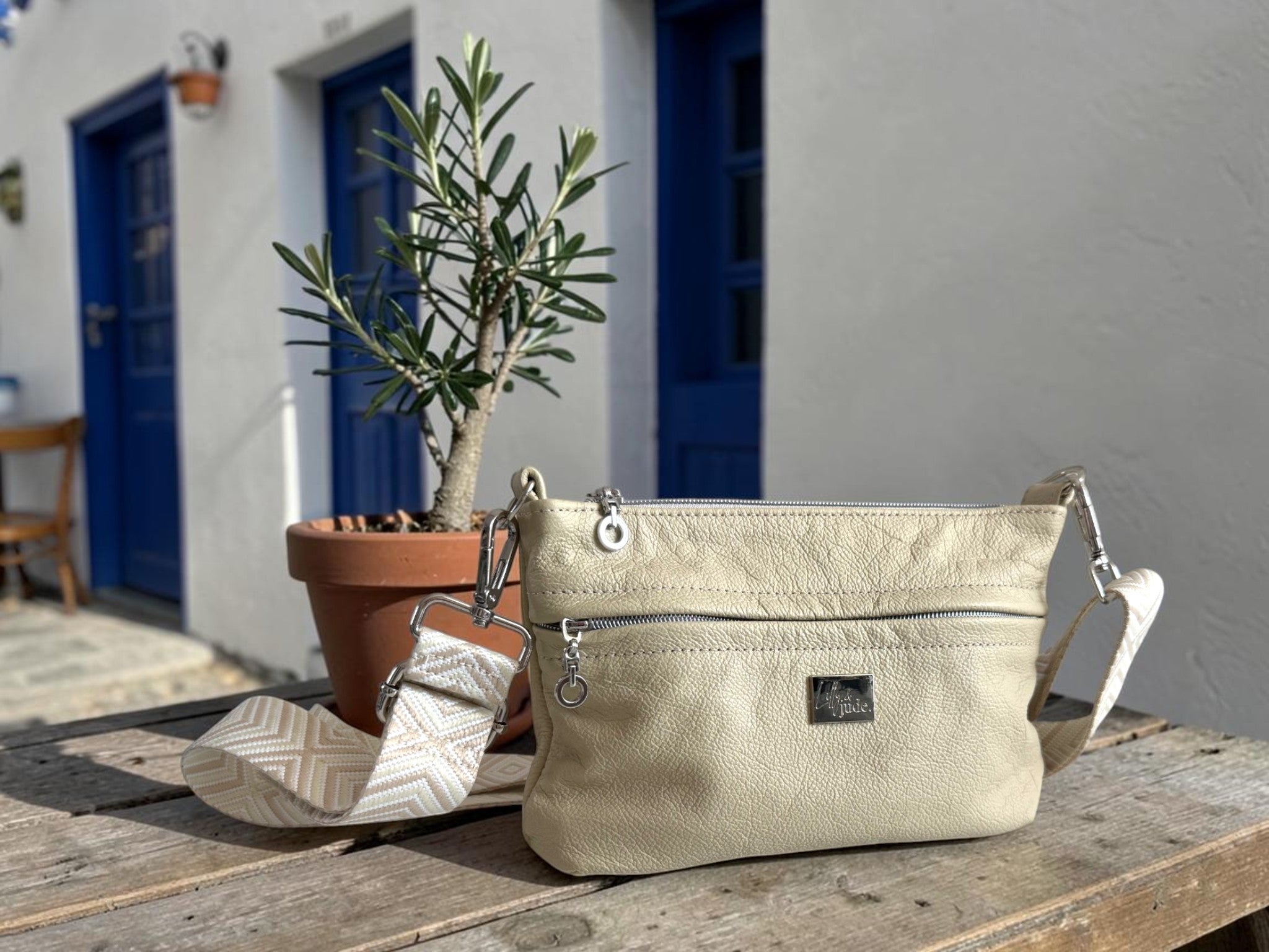 Cream leather crossbody bag with silver hardware and matching strap, sitting on a table outside a Greek Taverna