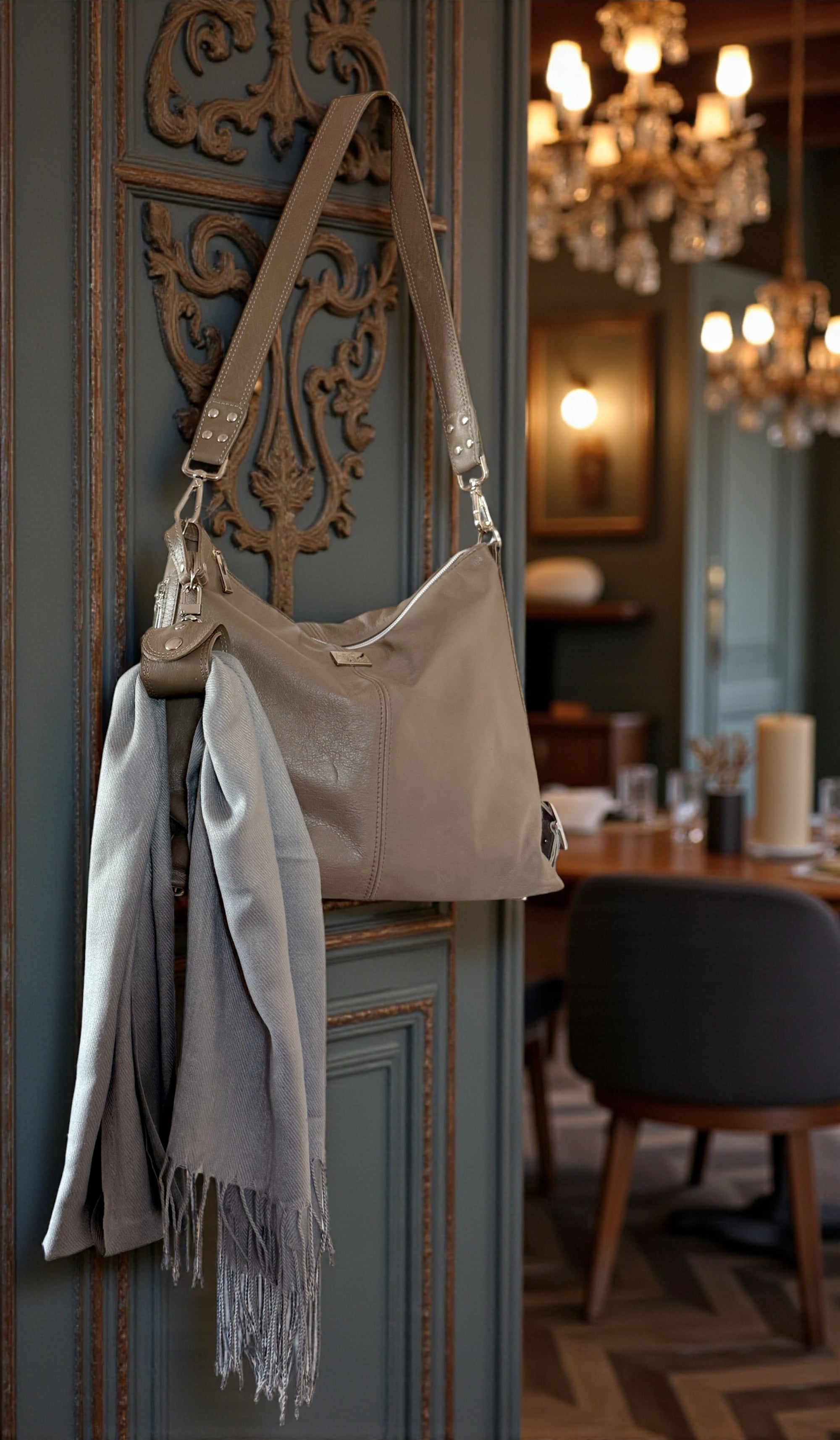 Beige handbag with a scarf draped through an accessory cuff, against an ornate wall.