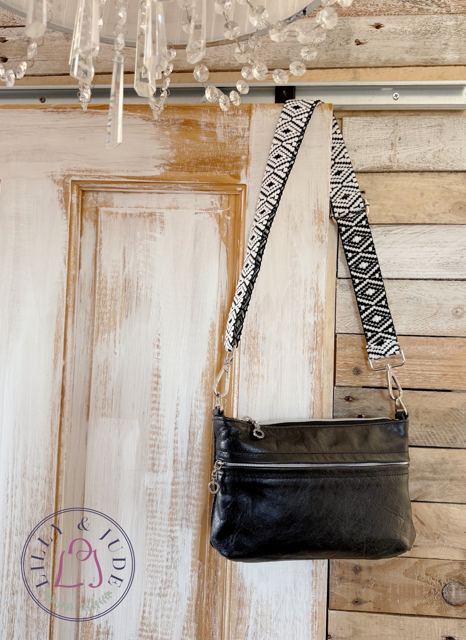 Black leather crossbody bag with a patterned strap hanging on a wooden door