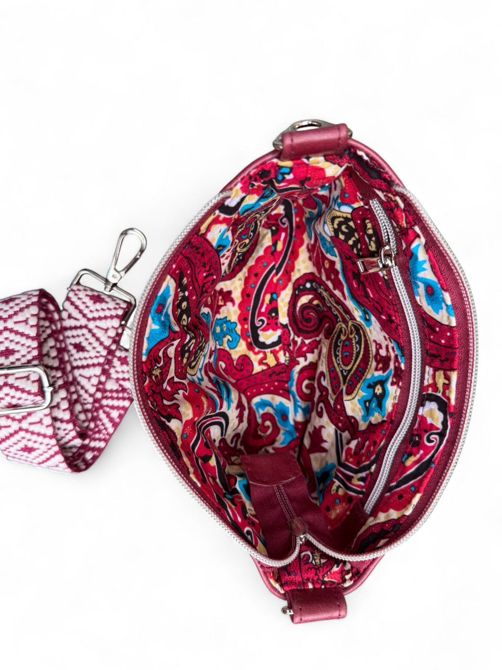 Birds Eye view of the open Starburn bag, showing the vibrant paisley lining. The matching woven crossbody strap in lying next to the bag on a white background