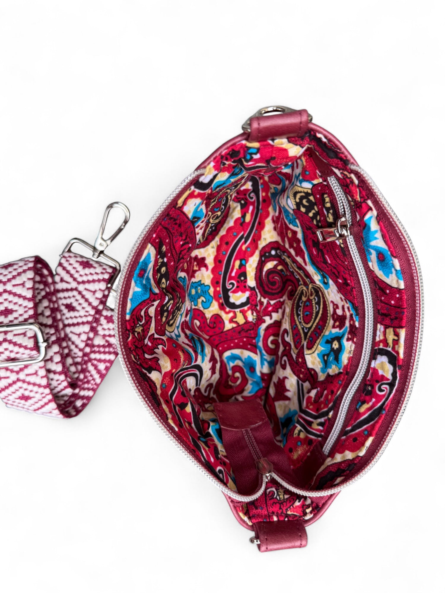Birds Eye view of the open Starburn bag, showing the vibrant paisley lining. The matching woven crossbody strap in lying next to the bag on a white background