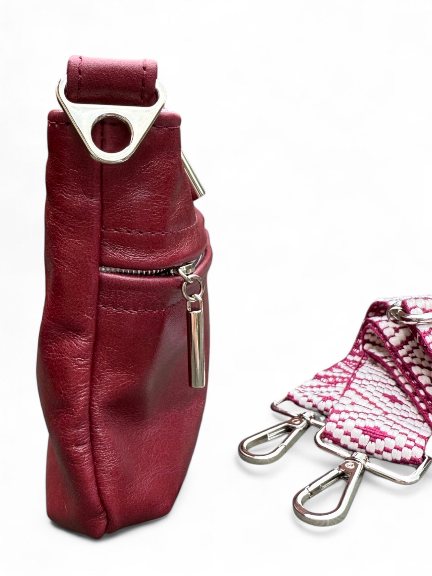Side view of deep red leather pouch with metal clasp and red and white patterned strap on a white background