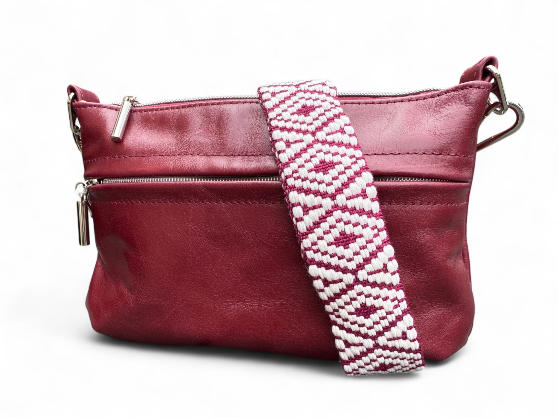 Burgundy coloured leather handbag with a white and burgundy patterned strap on a white background