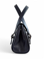 Side view of a navy blues leather handbag with a white background