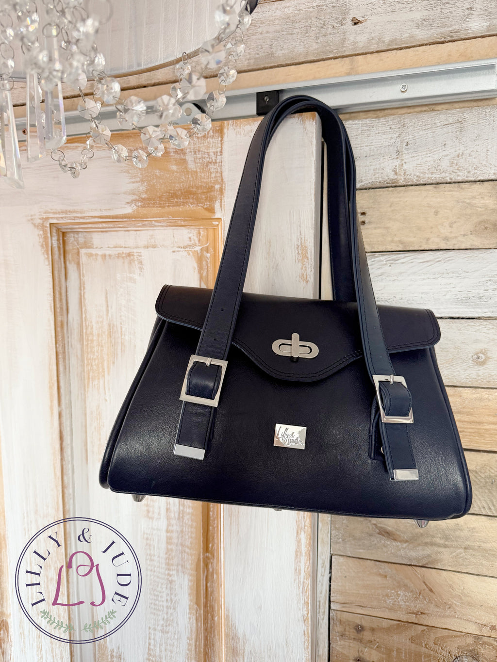 Navy blue handbag hanging on a wooden wall with a chandelier in the background.