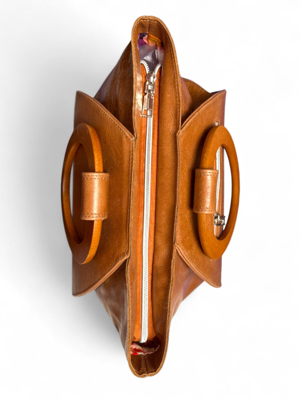 A birdseye view of the top of the Tricia handbag. The bag is made from tan coloured leather that was rescued from heading to landfill, and has matching wooden handles. Handcrafted by Lilly & Jude in the UK