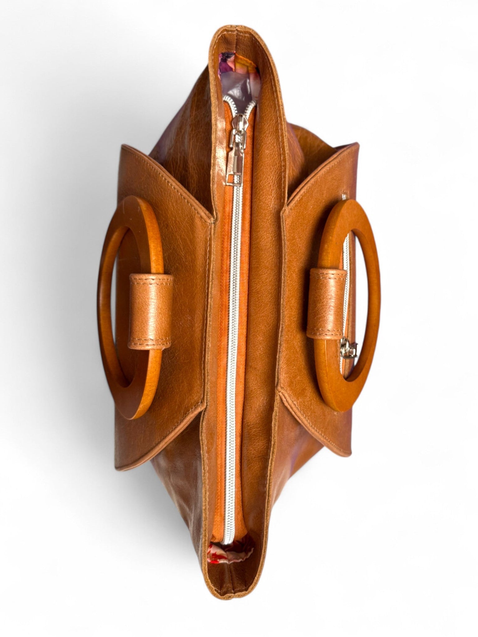 A birdseye view of the top of the Tricia handbag. The bag is made from tan coloured leather that was rescued from heading to landfill, and has matching wooden handles. Handcrafted by Lilly & Jude in the UK