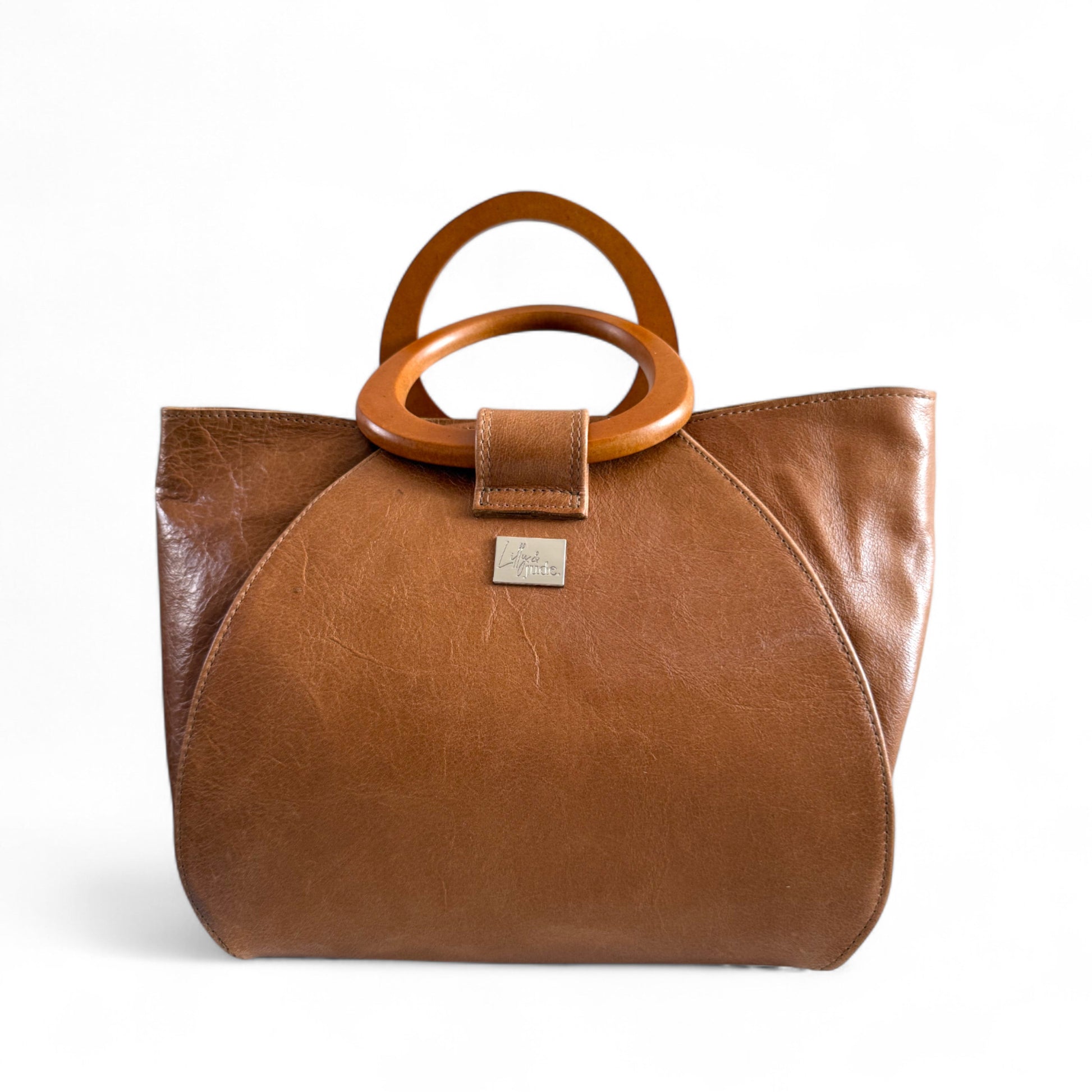 Tan leather handbag with wooden handles on a white background, handcrafted by Lilly & Jude in the UK.
