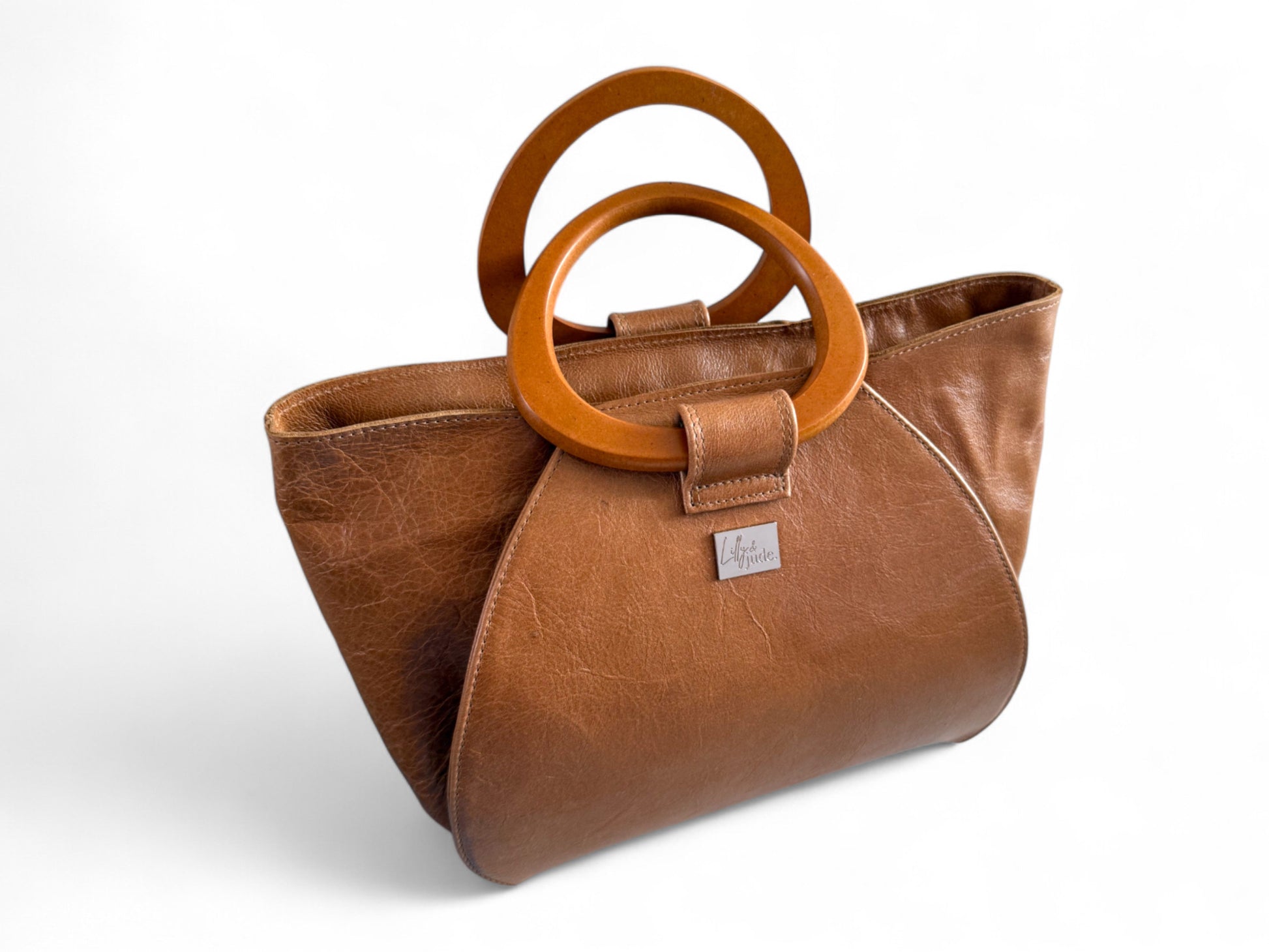 Tan brown leather handbag with wooden handles on a white background. The bag is called Tricia and is handcrafted in the UK by Kerry at Lilly & Jude