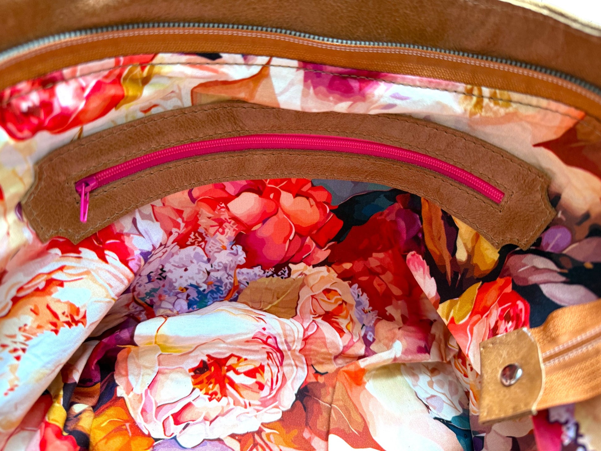Tricia handbag interior view, shows the floral printed lining fabric, and the leather trimmed zipper pocket with hot pink zipper. The bag is made from eco-conscious materials, including tan coloured leather that has been rescued from heading to landfill. Exclusive to Lilly & Jude