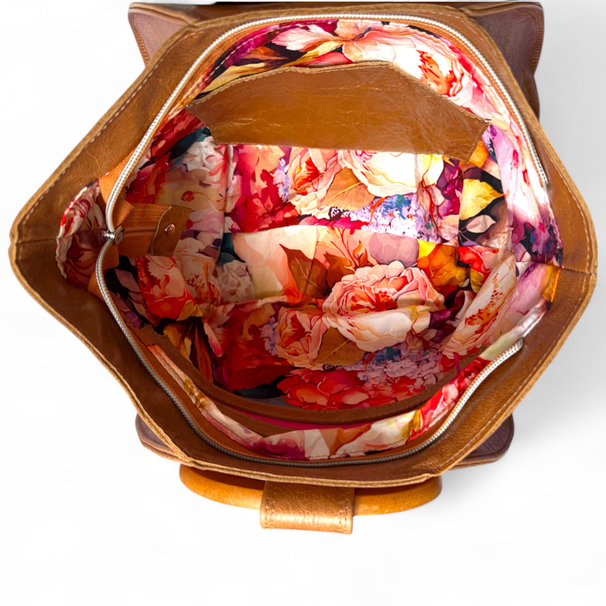 Floral-patterned fabric inside a tan coloured leather bag on a white background. The view is from above the Tricia handbag, shows the wide mouth opening of the bag. The bag is an eco-conscious option as it is hand made using leather that has been rescued from heading to landfill.