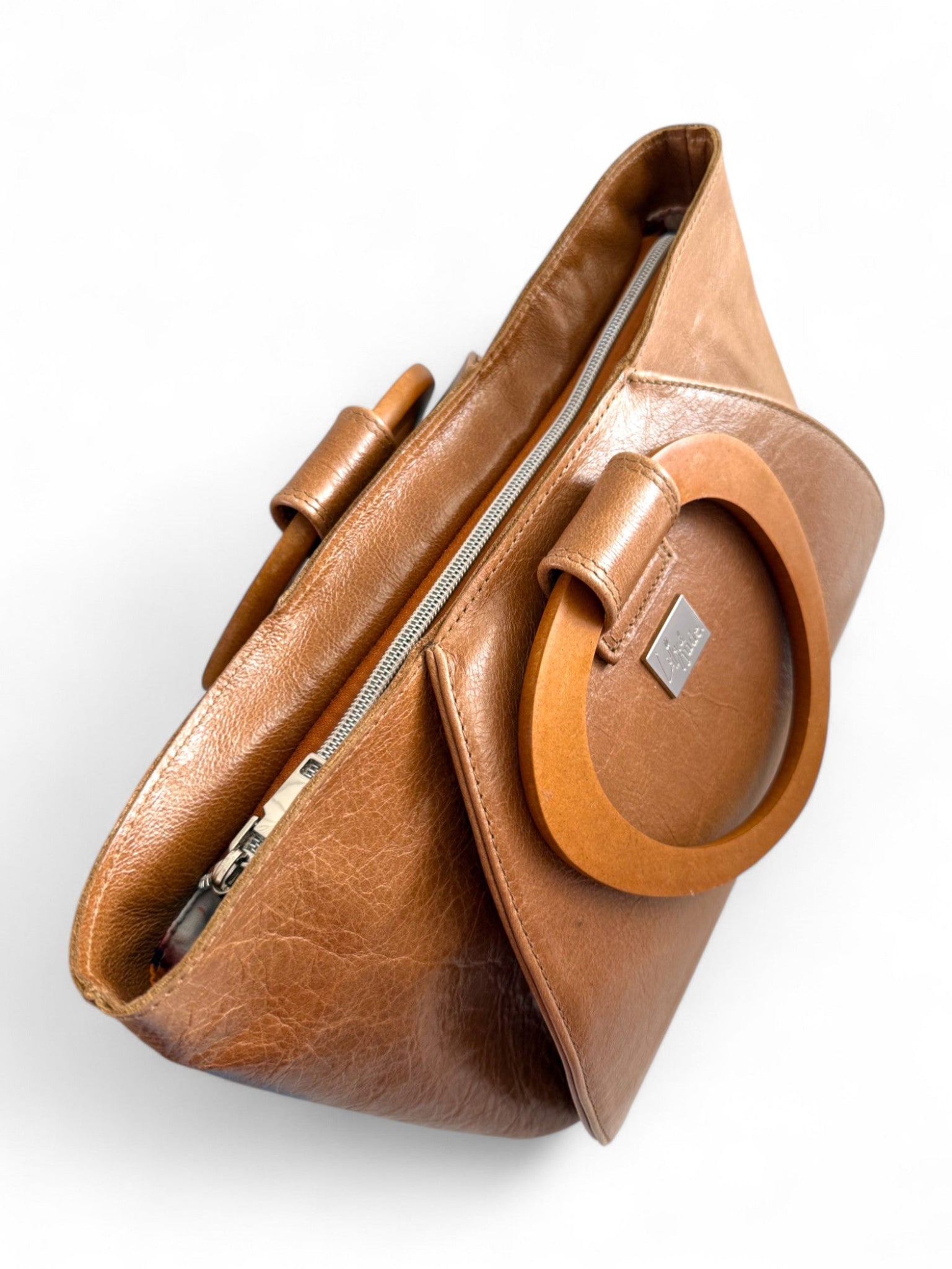 Tan brown leather handbag with wooden handles and  a visible 'Lilly & Jude'  brand logo on a white background. The view shows the top of the bah, with it's zippered closure