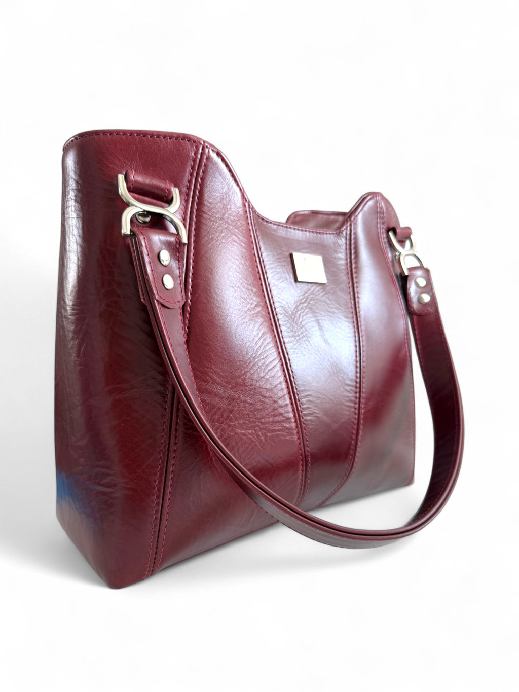 Deep red handbag with a shoulder strap on a white background. The image highlights the texture of the genuine rescued leather and the silver hardware