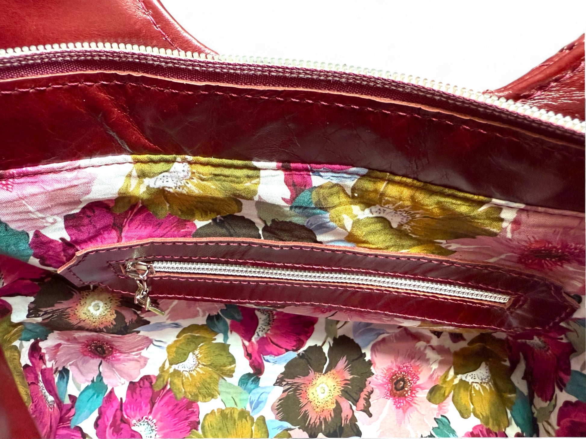 Interior view of the burgundy leather Alaula handbag by Lilly & Jude. The image highlights the leather trimmed interior zipper pocket and the floral lining fabric