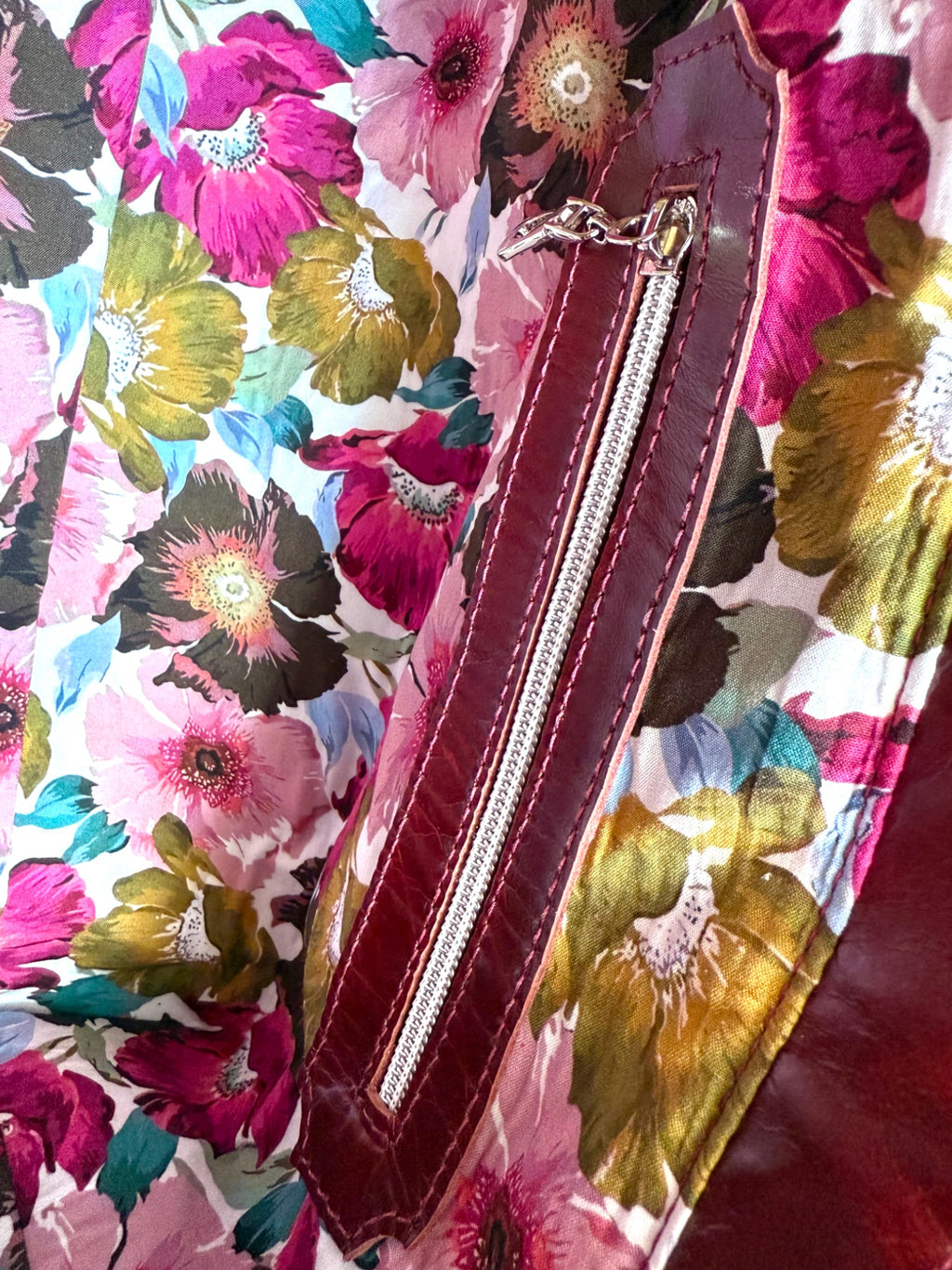 Interior view of the maroon leather Alaula handbag, highlighting the leather trimmed zipper pocket and floral lining fabric