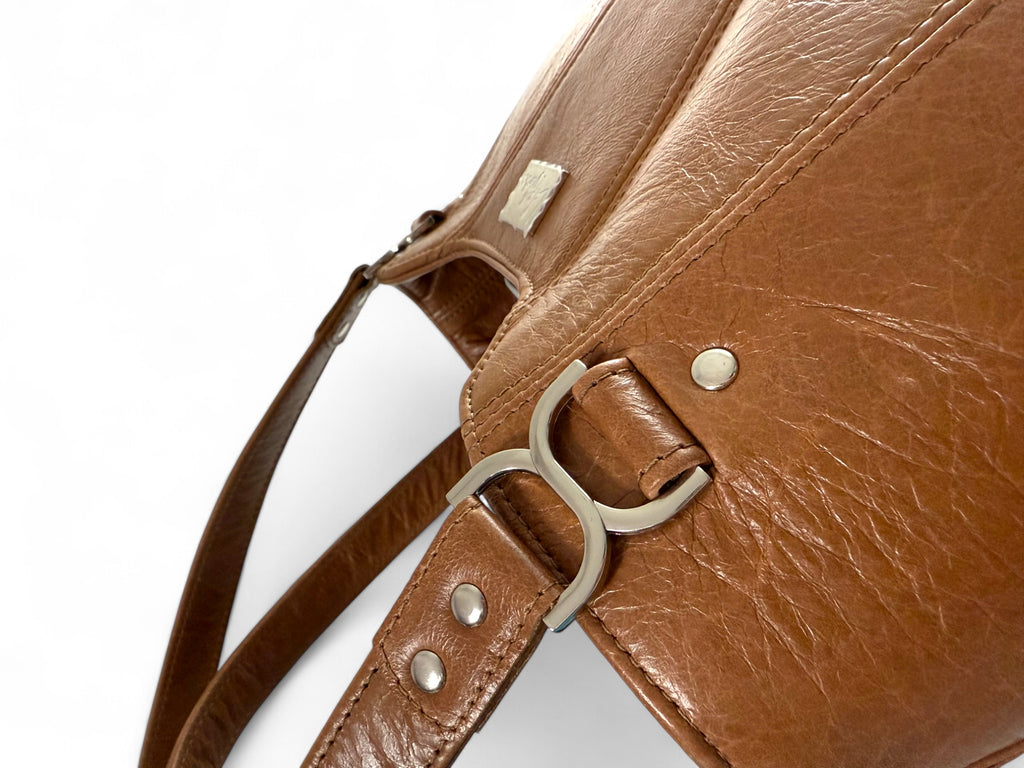 Close-up of the Alaula handbag in tan brown leather. The image shows the silver rivets, bag strap and the texture of the leather