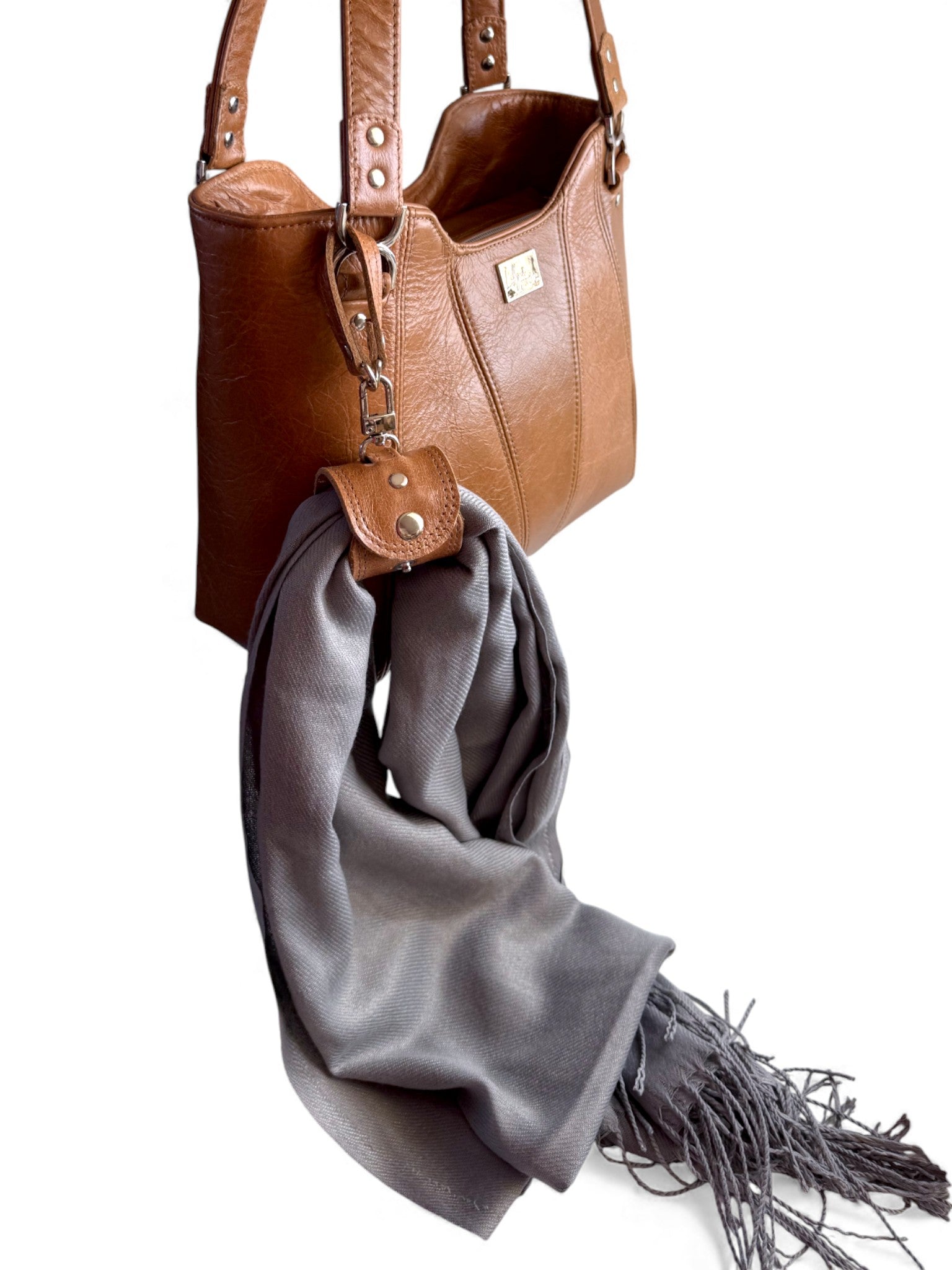 Tan leather handbag with the accessory strap, holding a grey scarf on a white background