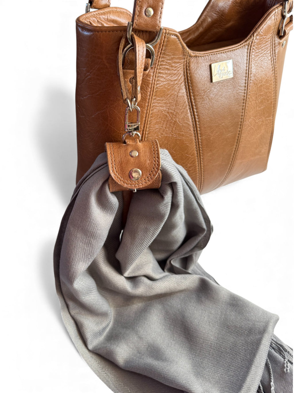 Tan brown leather handbag with a matching accessory cuff, holding a grey cashmere scarf, on a white background
