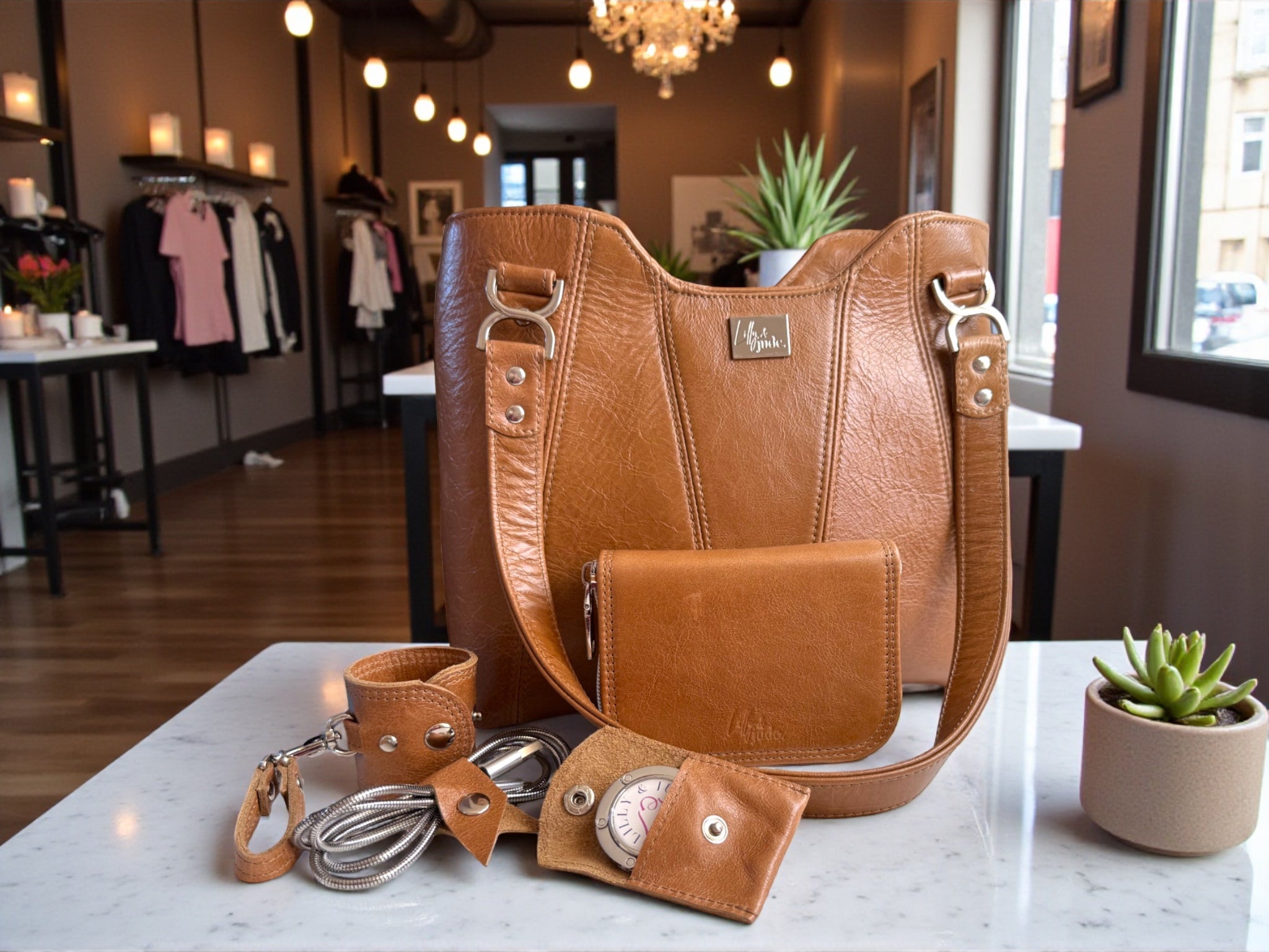 Brown leather handbag with matching wallet/purse, bag hook, accessory cuff  and cable keeper on a marble surface in a fashion boutique setting.