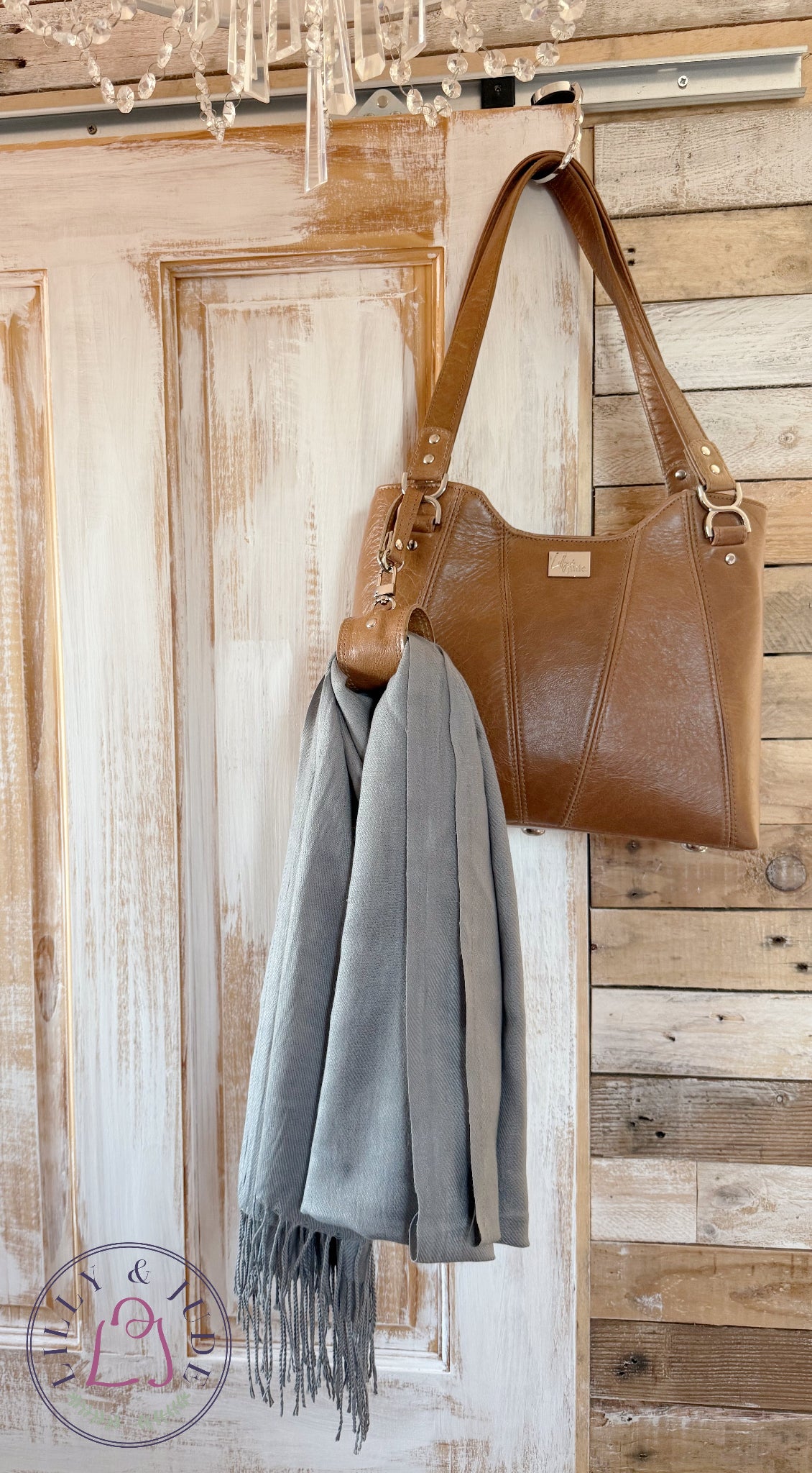 Brown leather handbag with a grey scarf hanging on a wooden door.