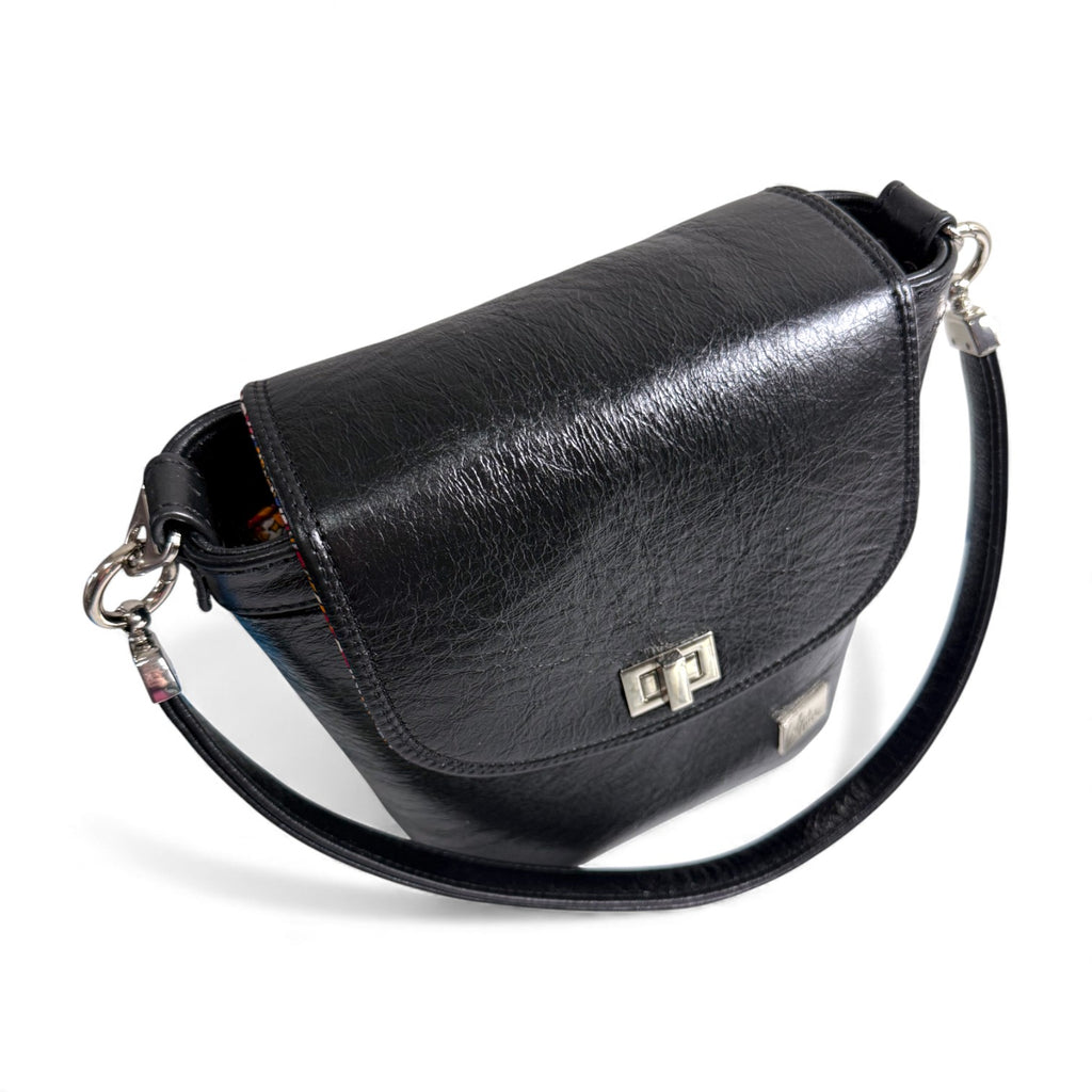 Top, front view of the Belle bucket bag, showing the silver twist lock on the front flap and hardware of the strap and connectors