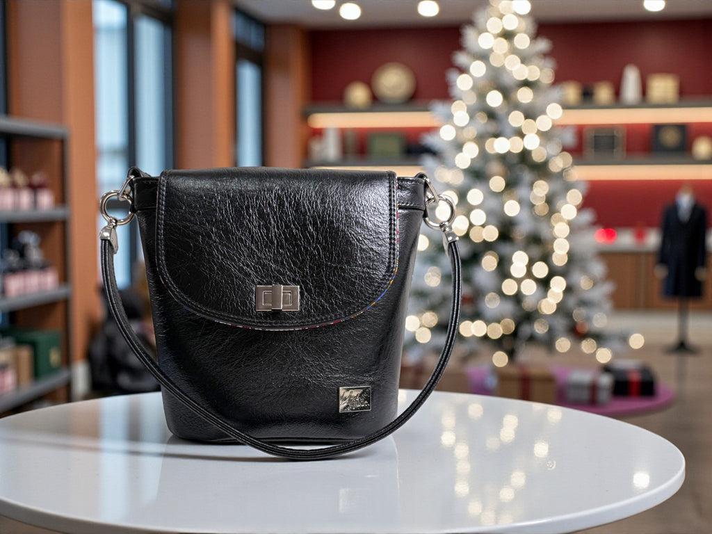 Black Belle bucket bag, made from black rescued leather, sitting on a white table in a boutique, with a beautifully lit Christmas tree in the background