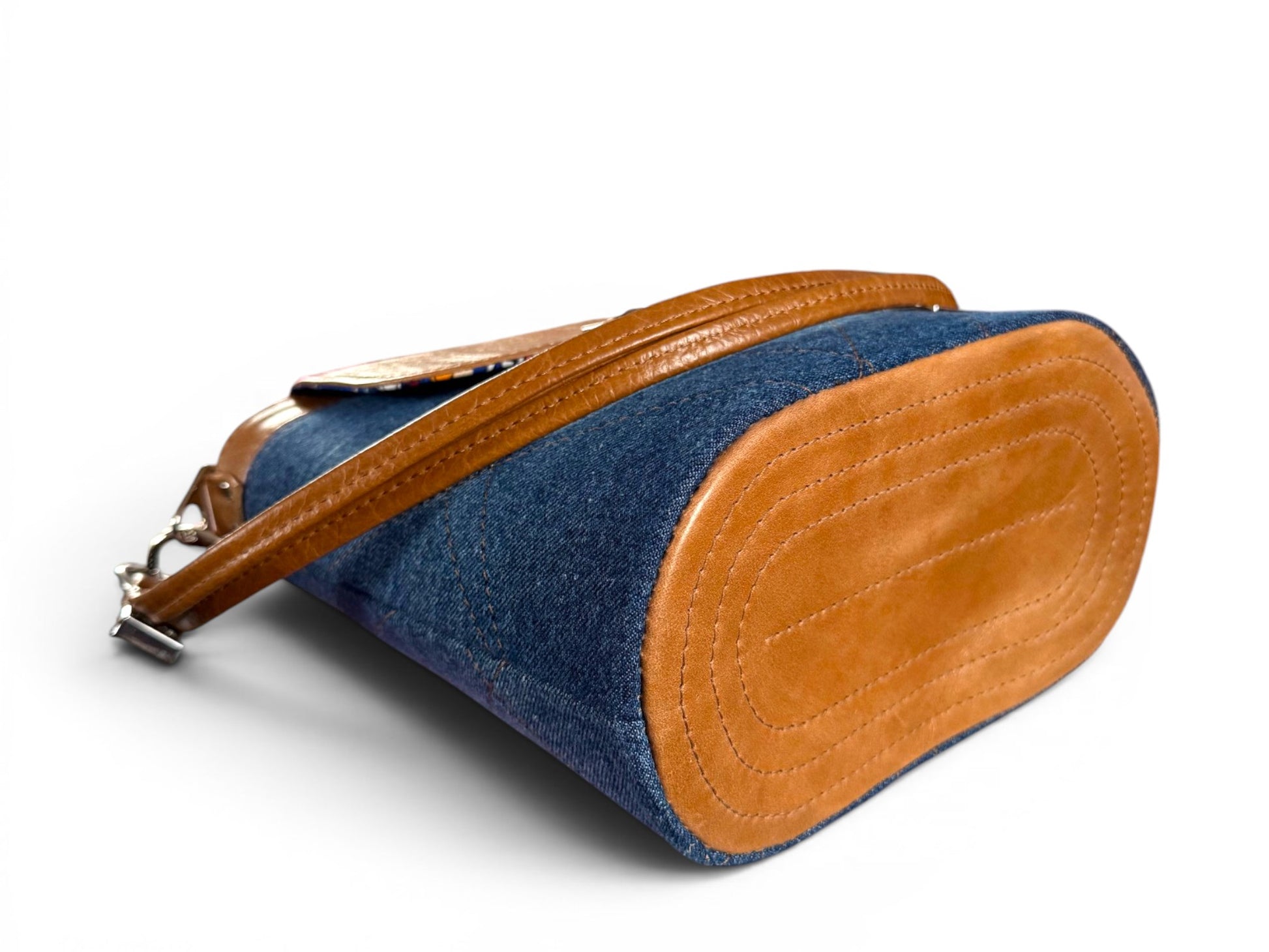 View of the bottom of the Belle Bucket Bag, a blue denim and tan brown leather handbag on a white background