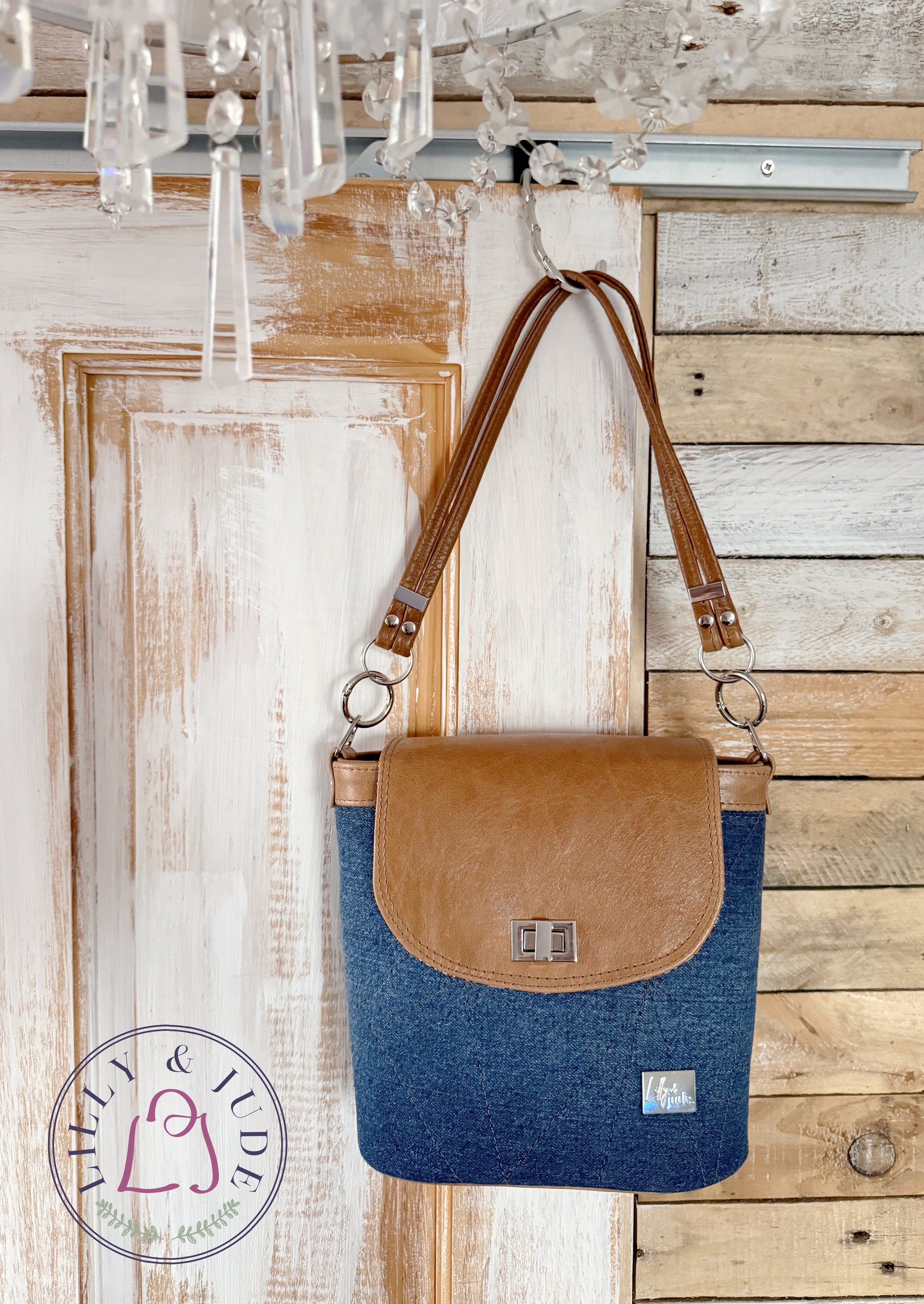 Blue denim and tan brown bucket bag, hanging on a wooden wall with a chandelier above.