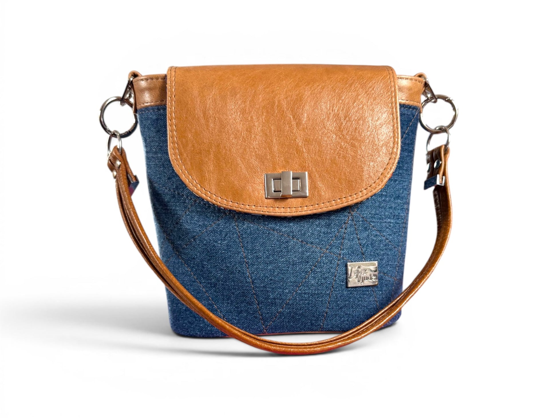 Blue denim bucket bag handbag with a tan brown leather flap and strap on a white background