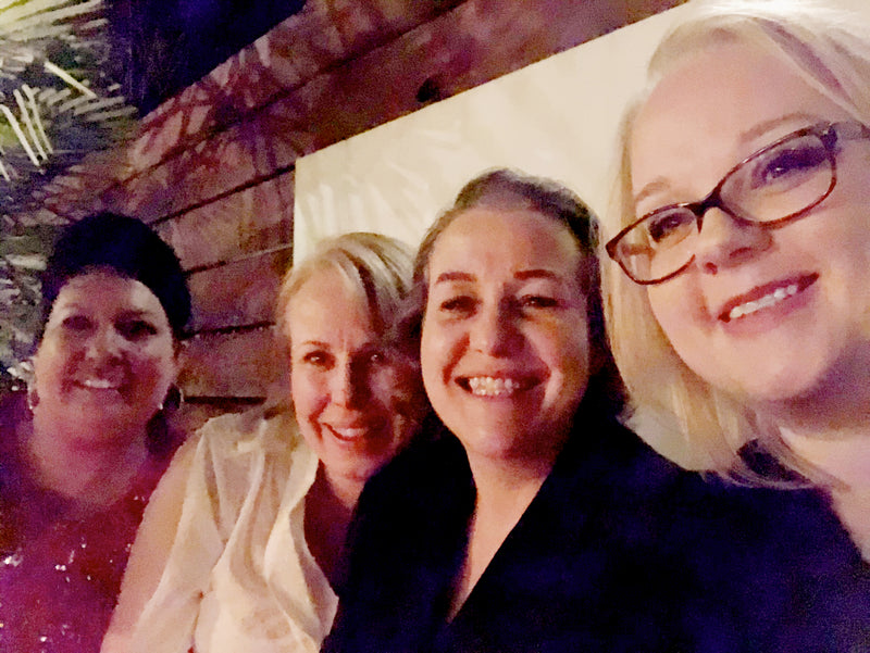Four women posing for a selfie in an outdoor setting with wooden beams.