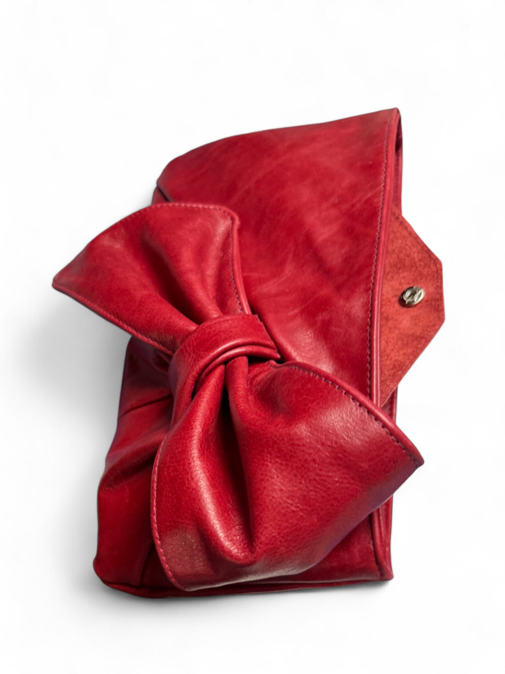 Red leather Betty Bow clutch bag, lying down on a white surface. The image is focussed on the large leather bow on the front and shows the flap of the integrated purse peeking out the top of the bag