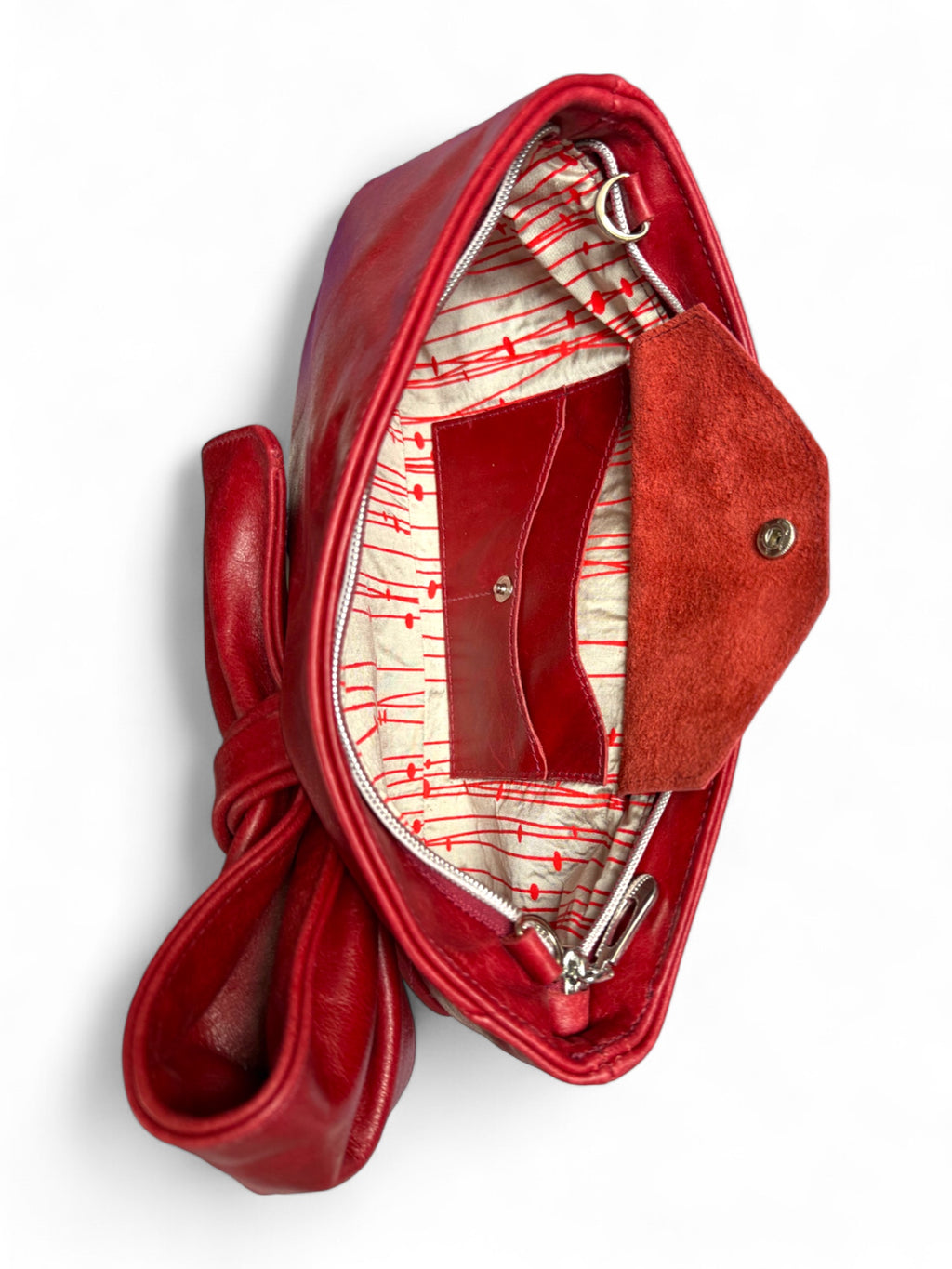 Red genuine leather clutch handbag with a red and champagne coloured, patterned silk interior lining and integrated purse, on a white background. Sustainable fashion, handcrafted in the UK 