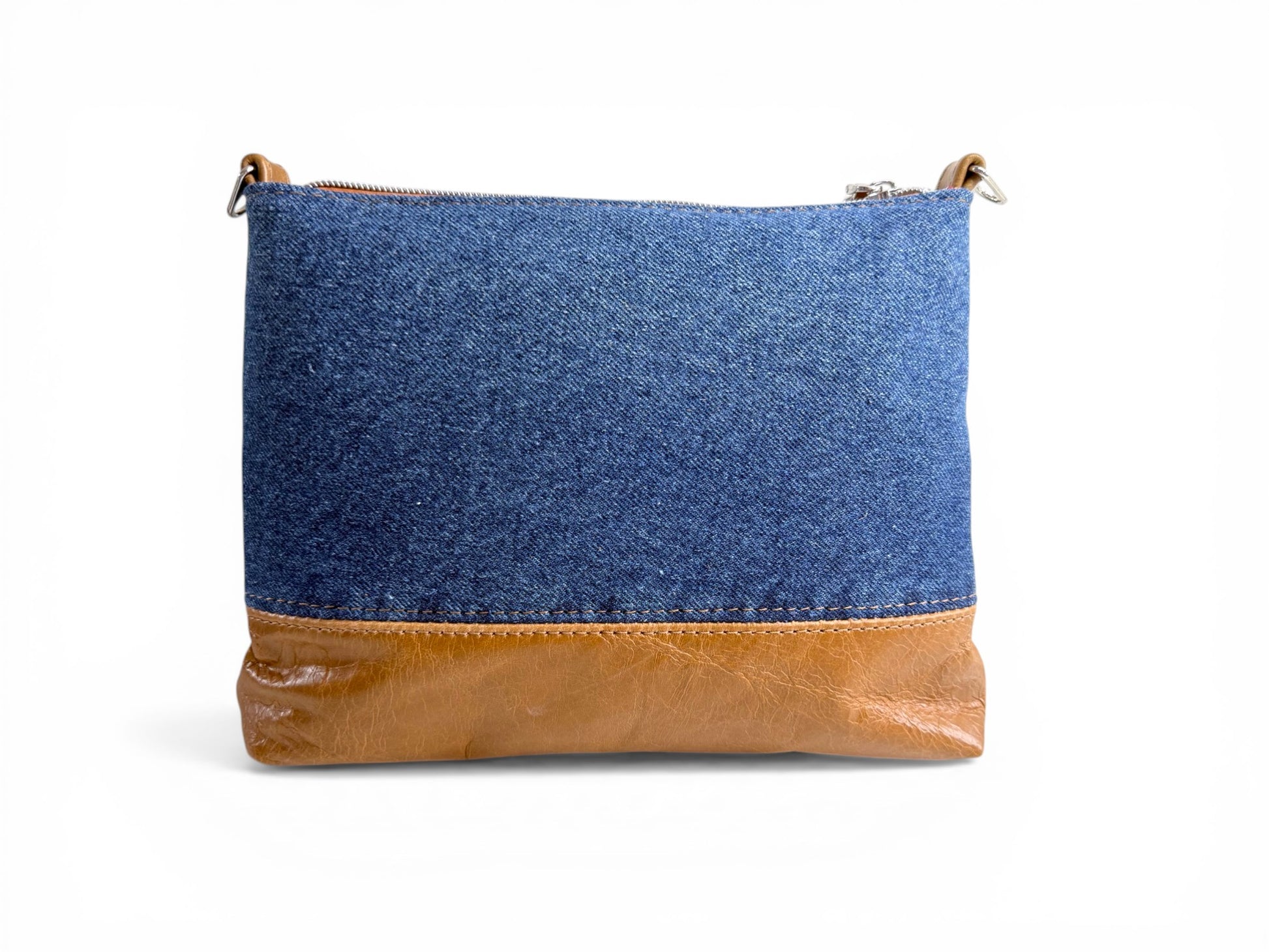 Rear view of the Bonny crossbody bag, made of blue denim with tan brown leather bottom on a white background