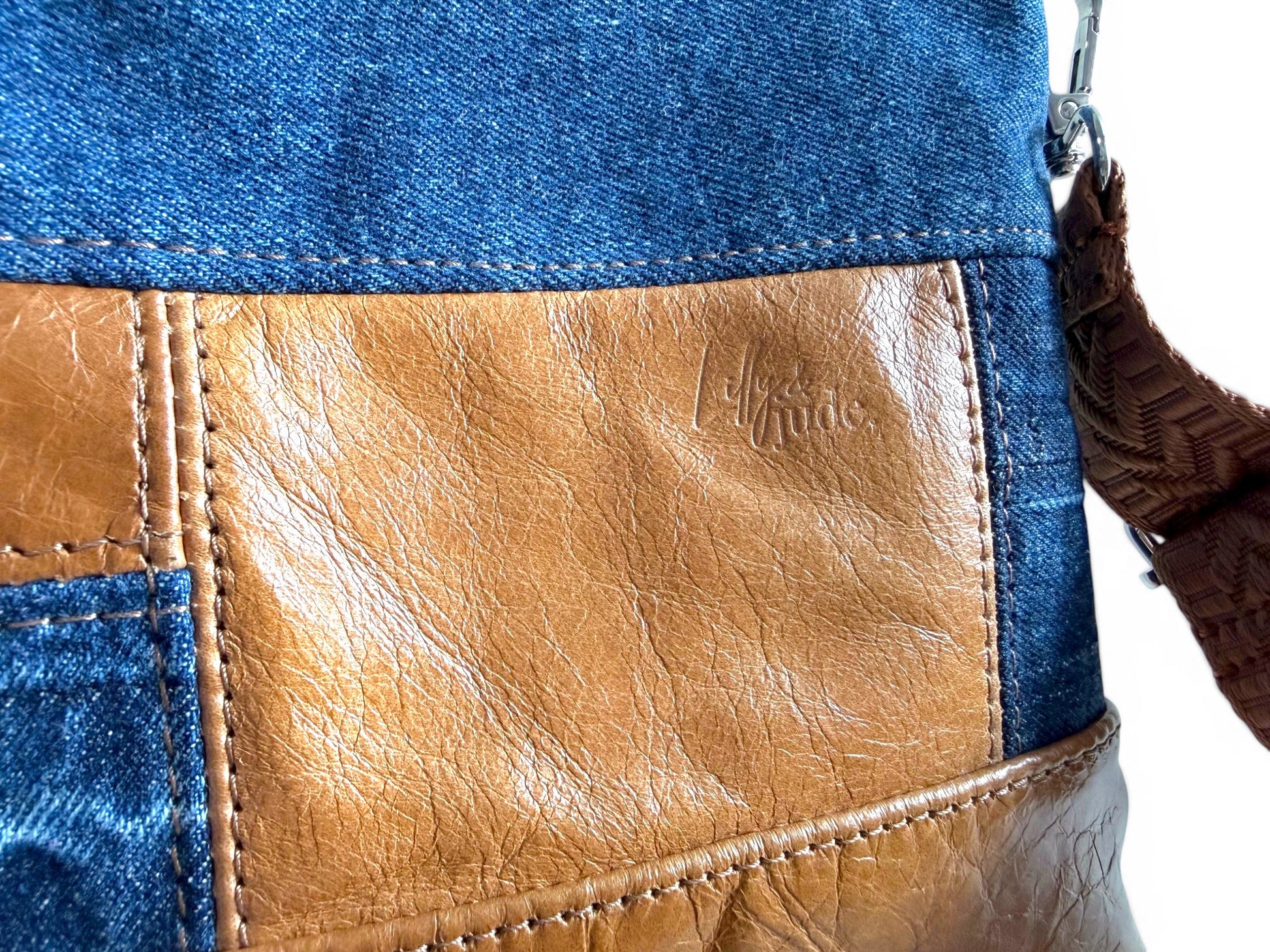 Close-up of a bag with denim and leather design, featuring a Lilly & Jude brand logo.
