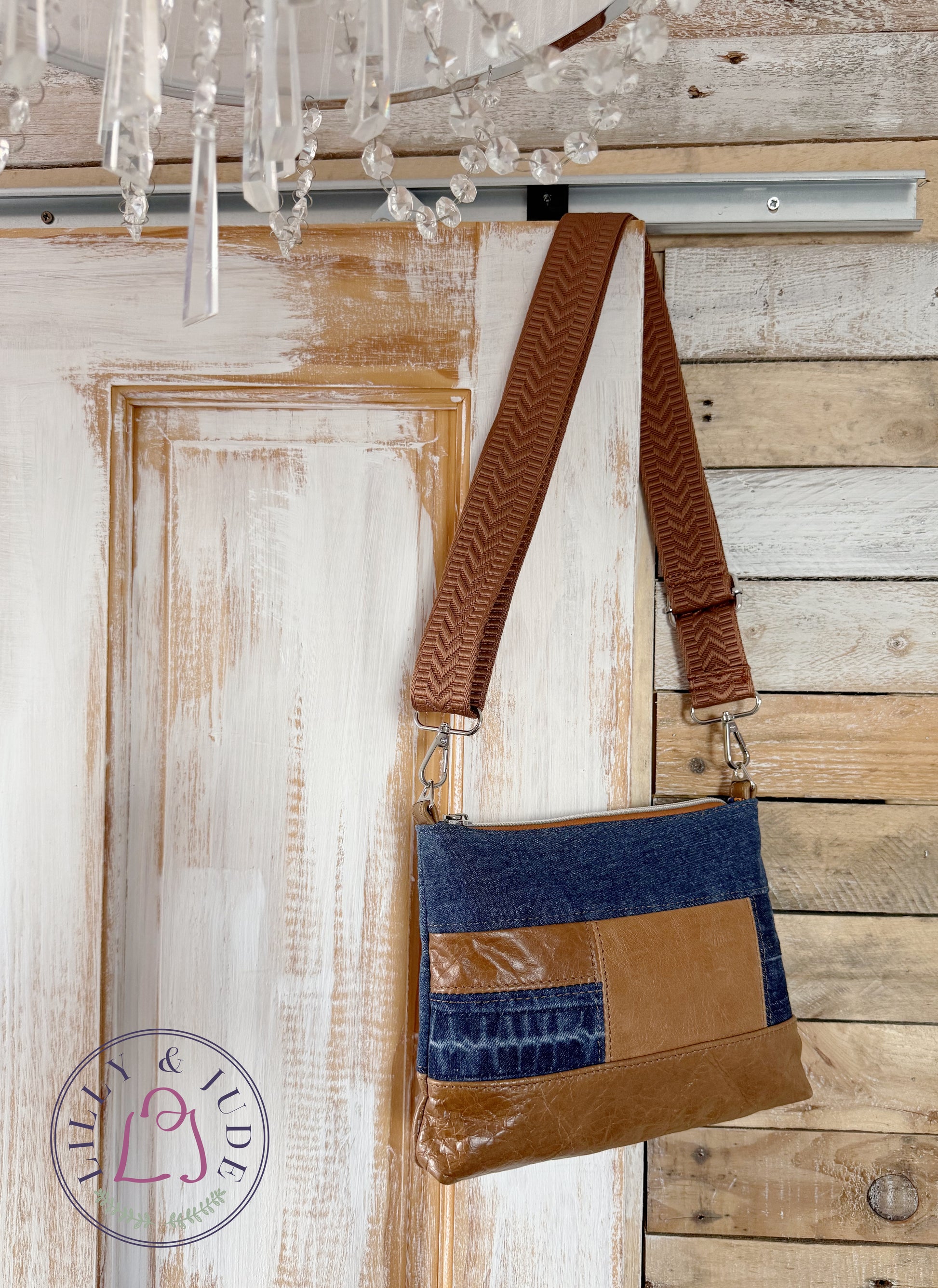 Patchwork handbag with tan brown leather and blue denim design hanging on a wooden door. The Lilly & Jude logo is affixed to the image